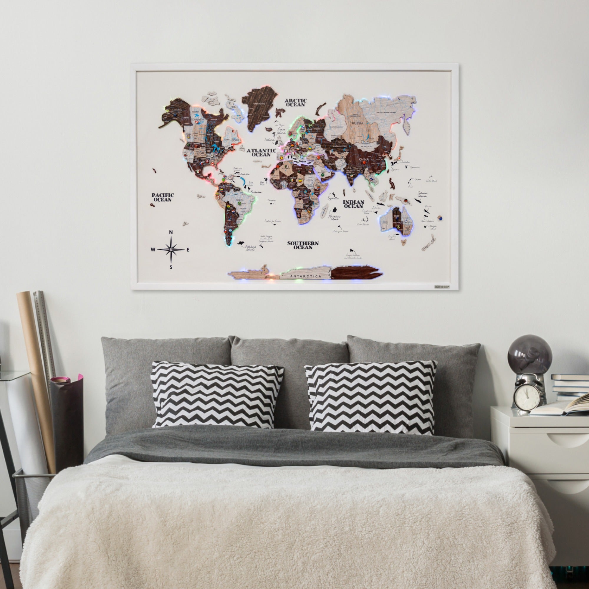 World map poster on a wall above a bed with decorative pillows.