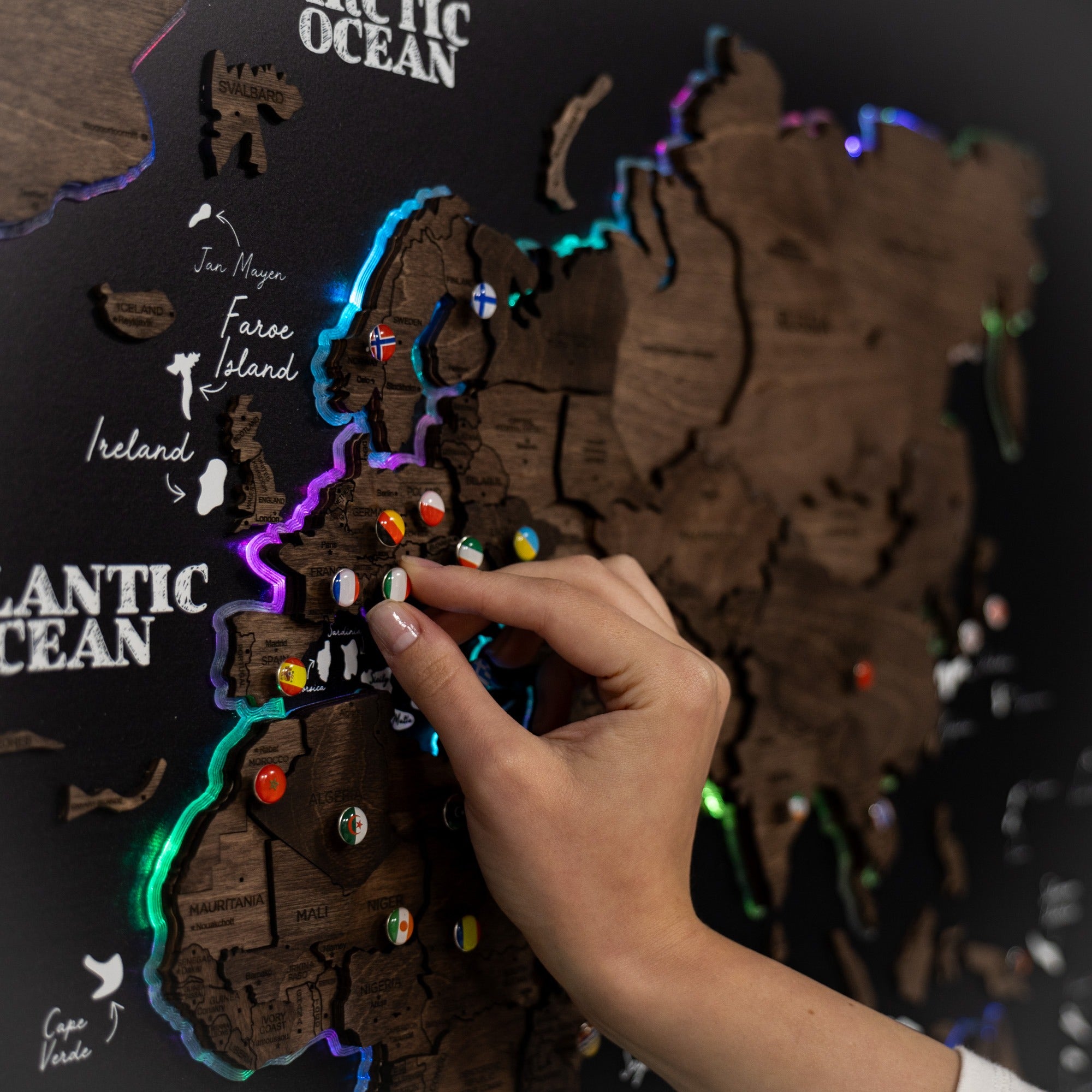 Hand interacting with a wooden map of Ireland featuring colorful pins on a dark background.