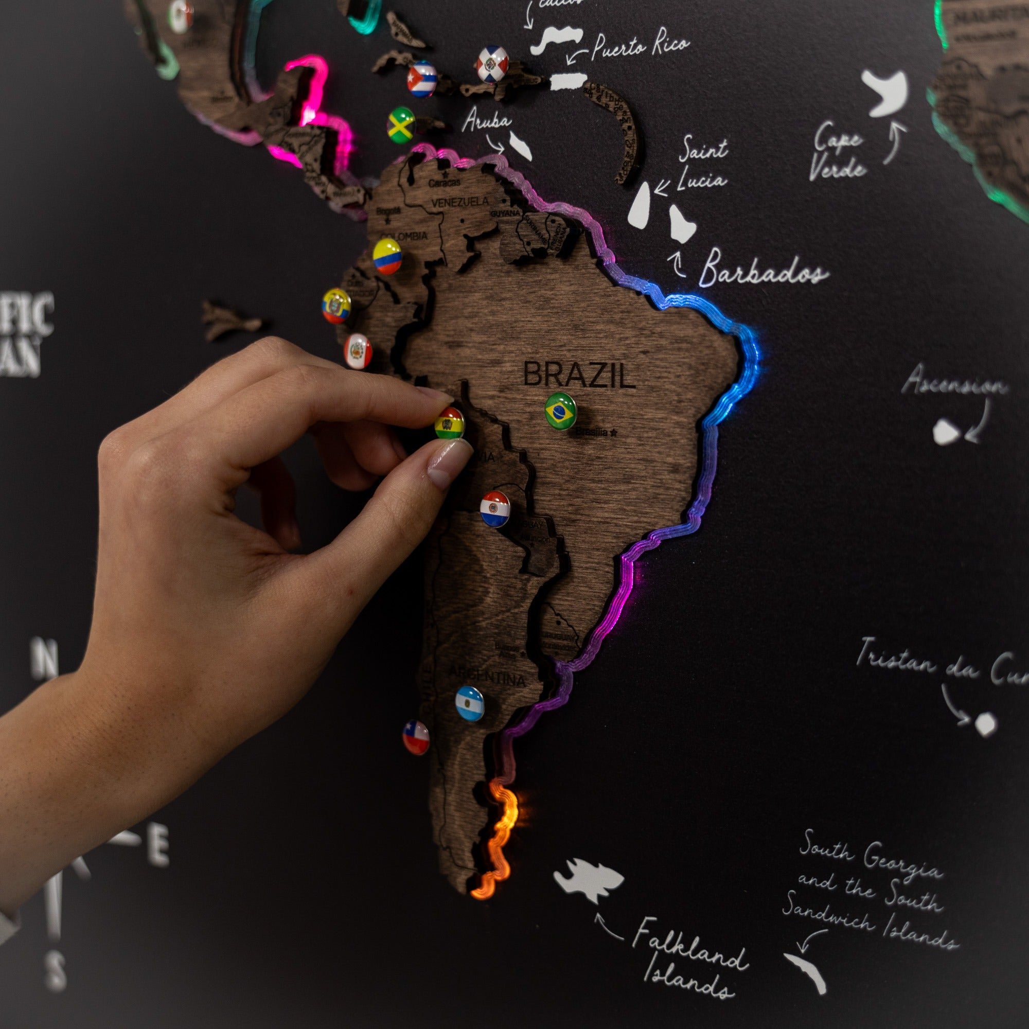 Hand placing a colorful pin on a wooden map of South America.