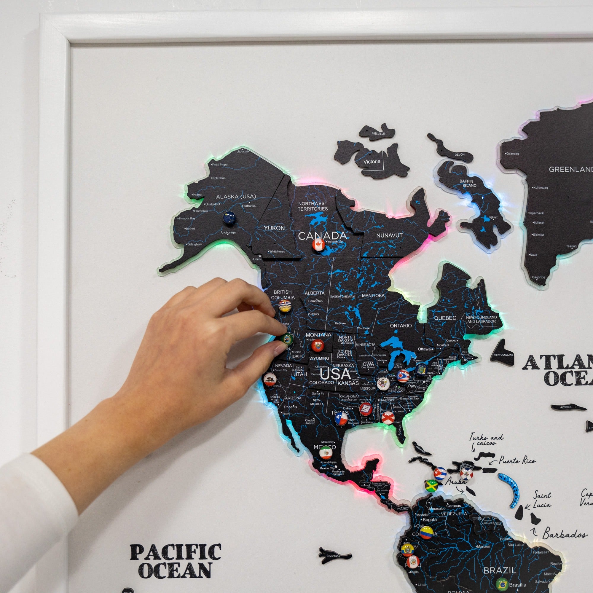 Map of North America with pins marking locations, held by a hand against a white background.