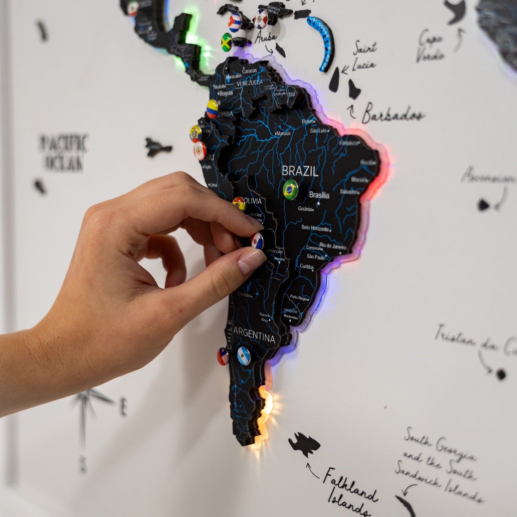 Hand holding a LED light-up map of Brazil against a whiteboard with geographical text.