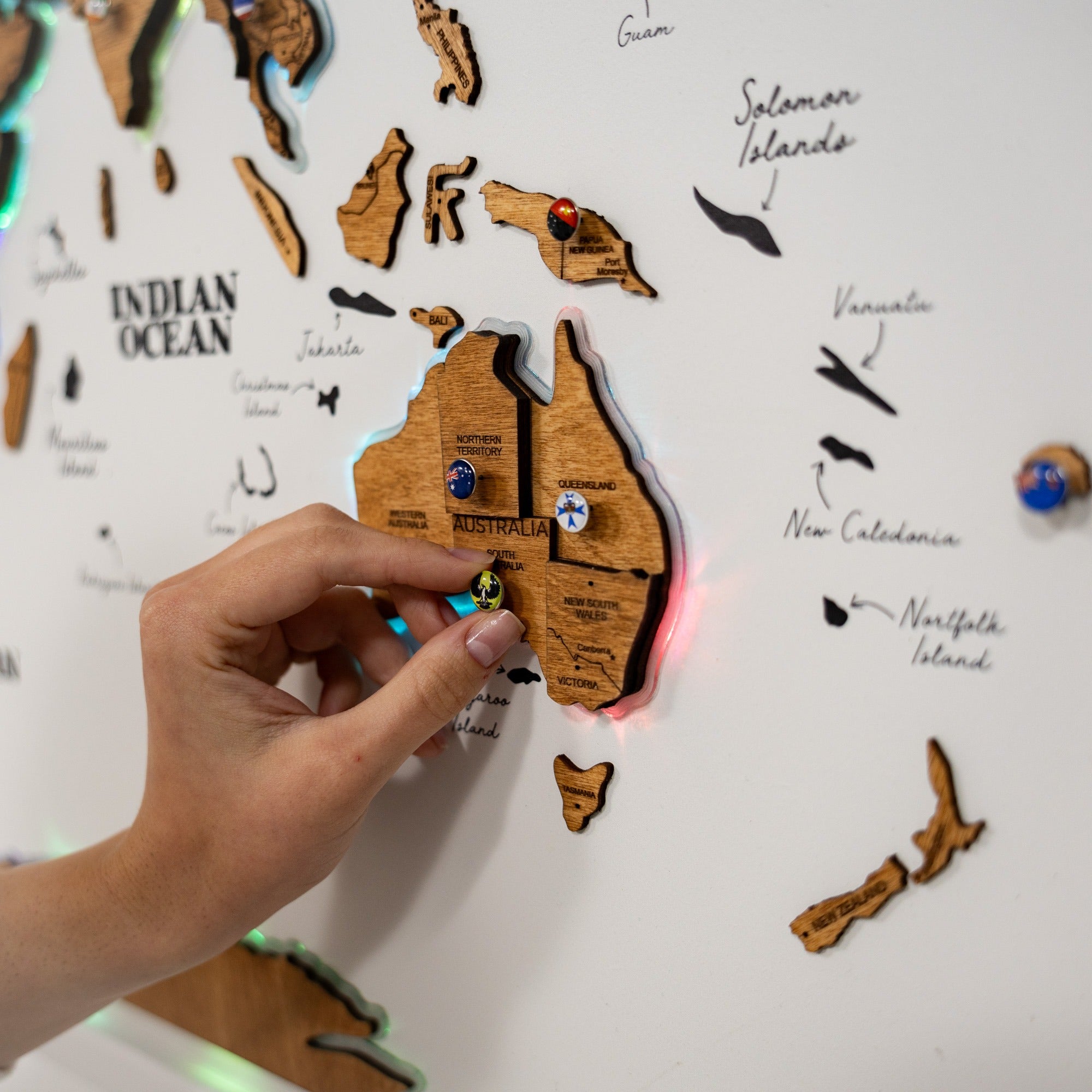 Wooden map of Australia on a white board with a hand pointing to it
