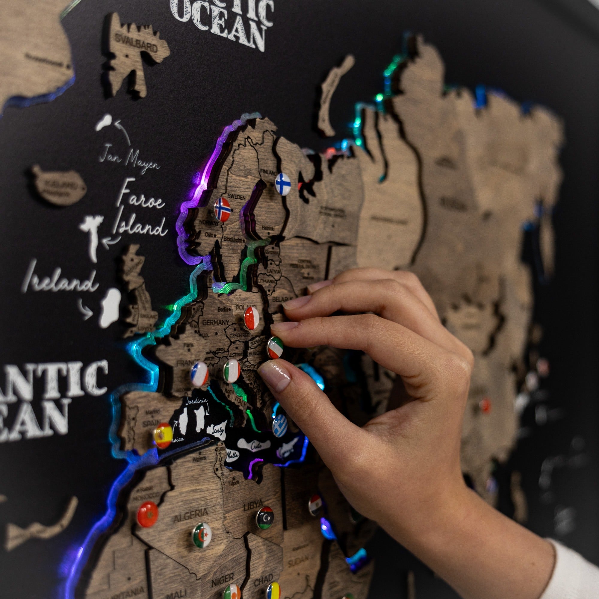 Hand interacting with a wooden map of Europe with LED lights and flags.