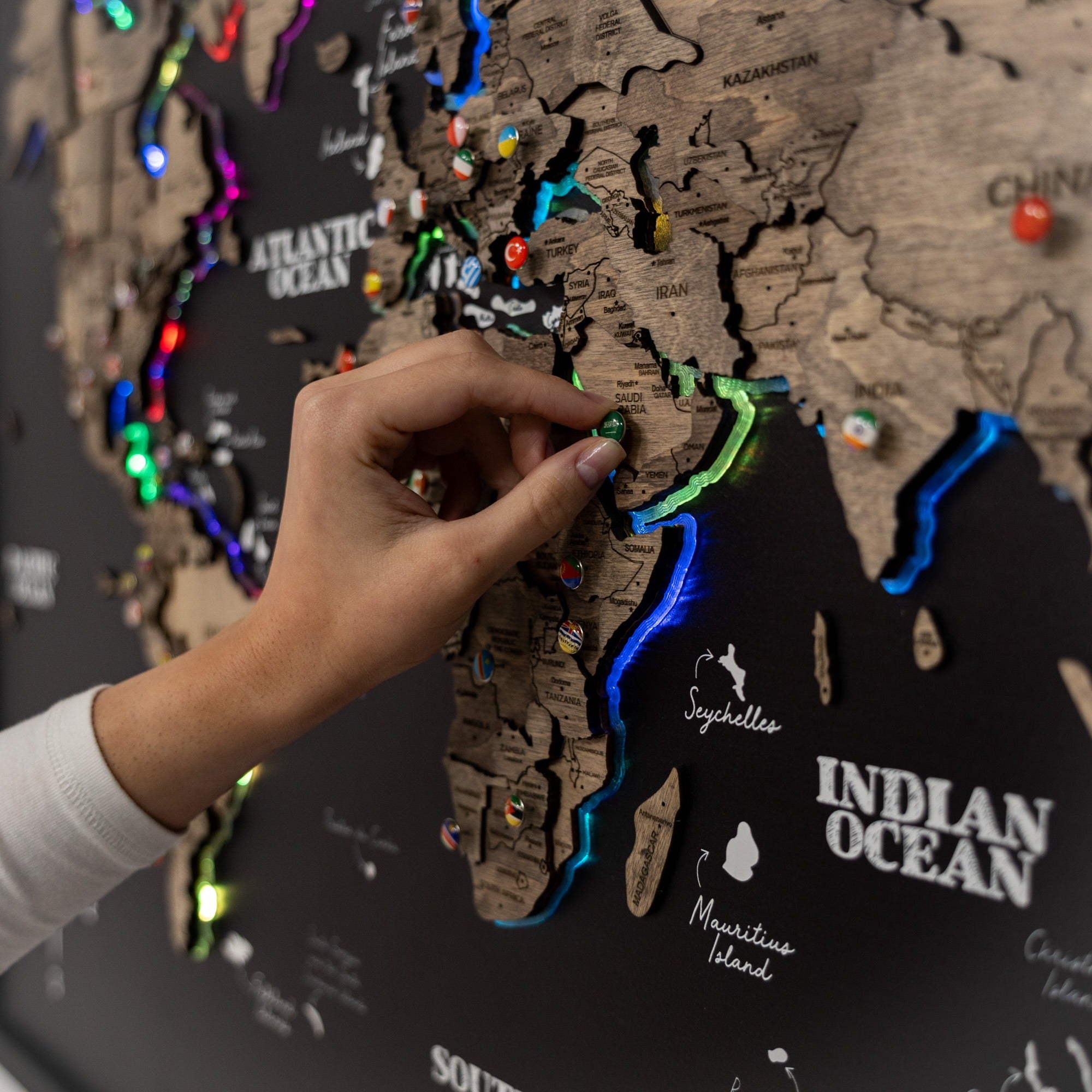 Hand placing a colorful pushpin on a wooden map of the world.