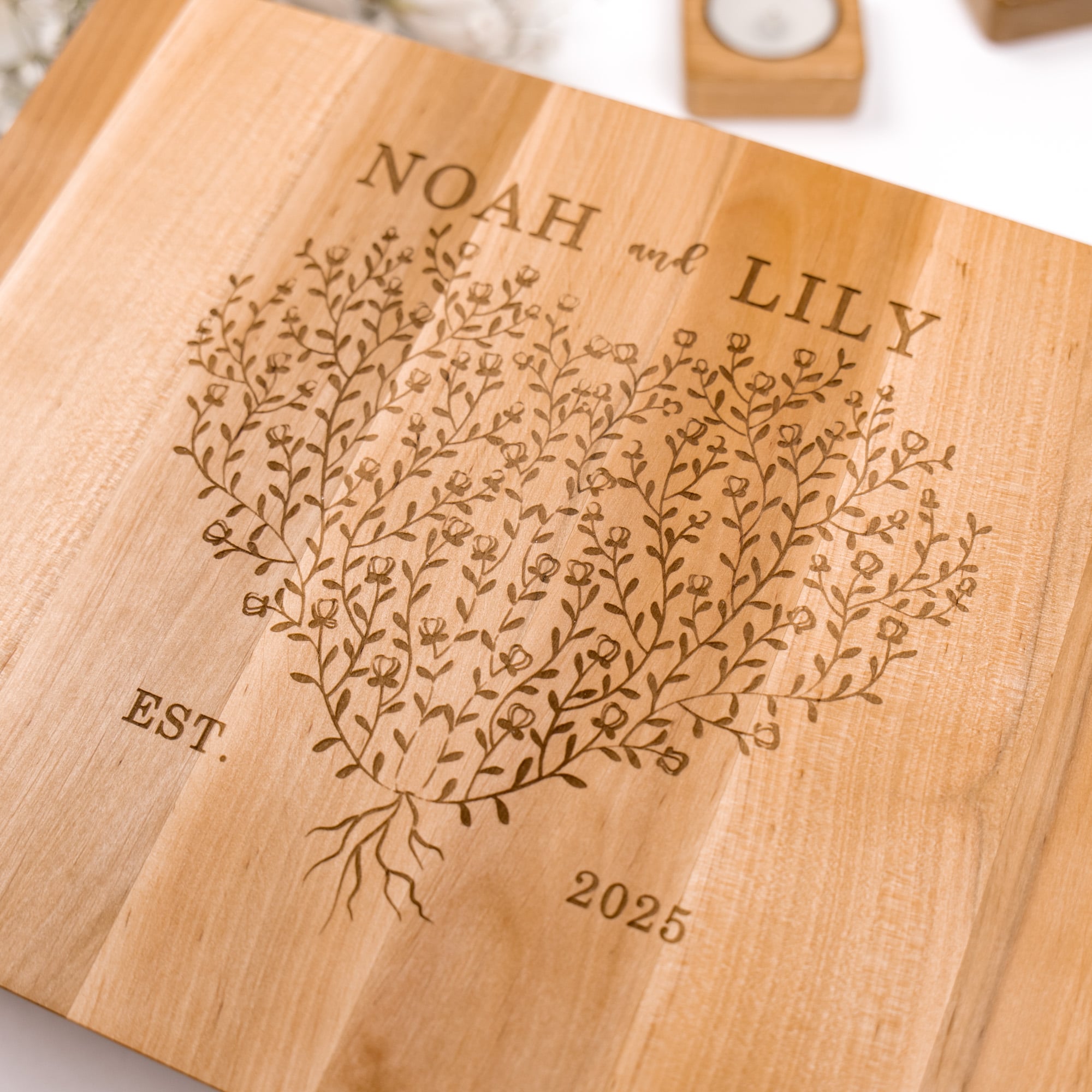 Wooden cutting board with engraved floral design and text 'NOAH and LILY EST. 2025'