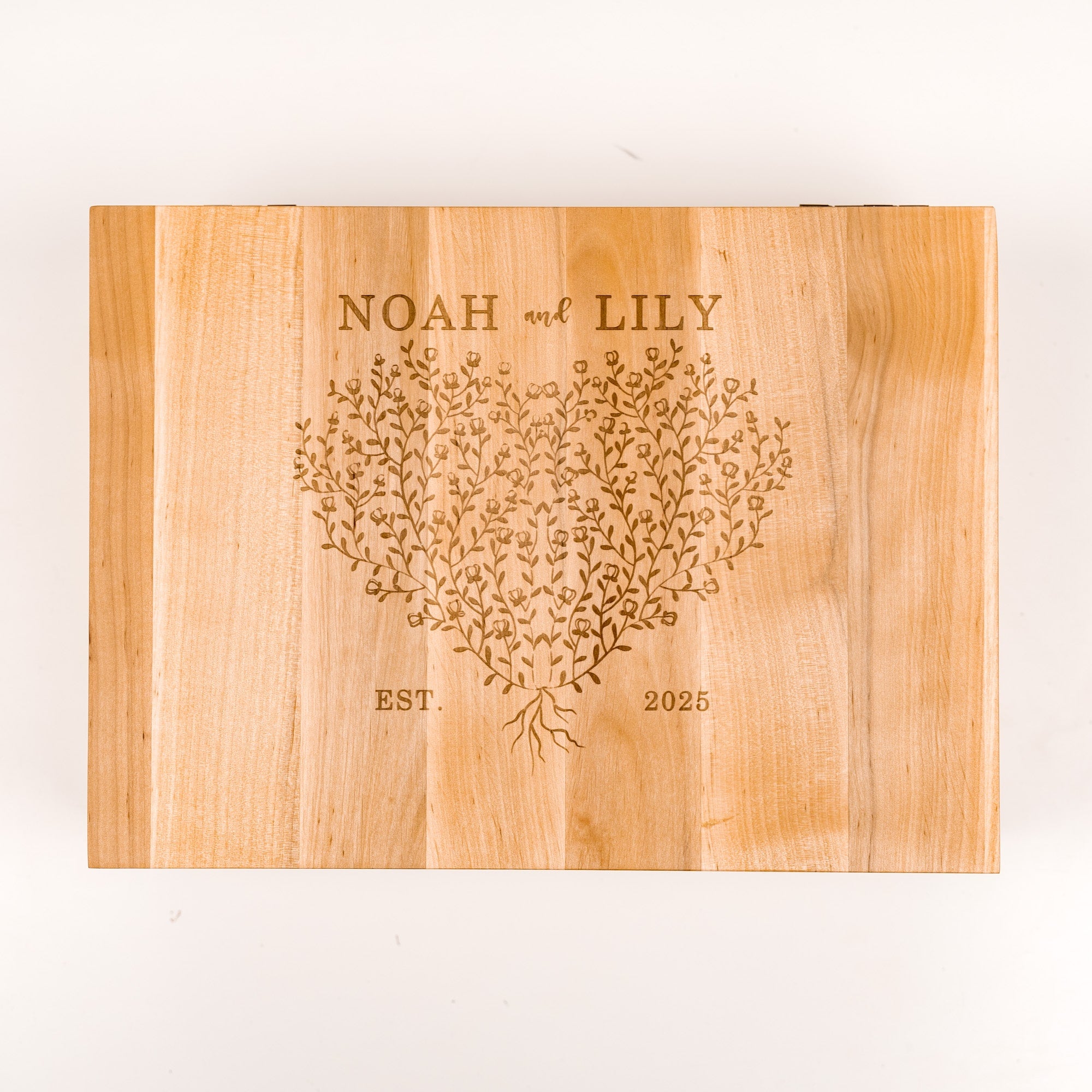 Wooden cutting board with engraved heart design and text 'NOAH and LILY EST. 2025' on a white background