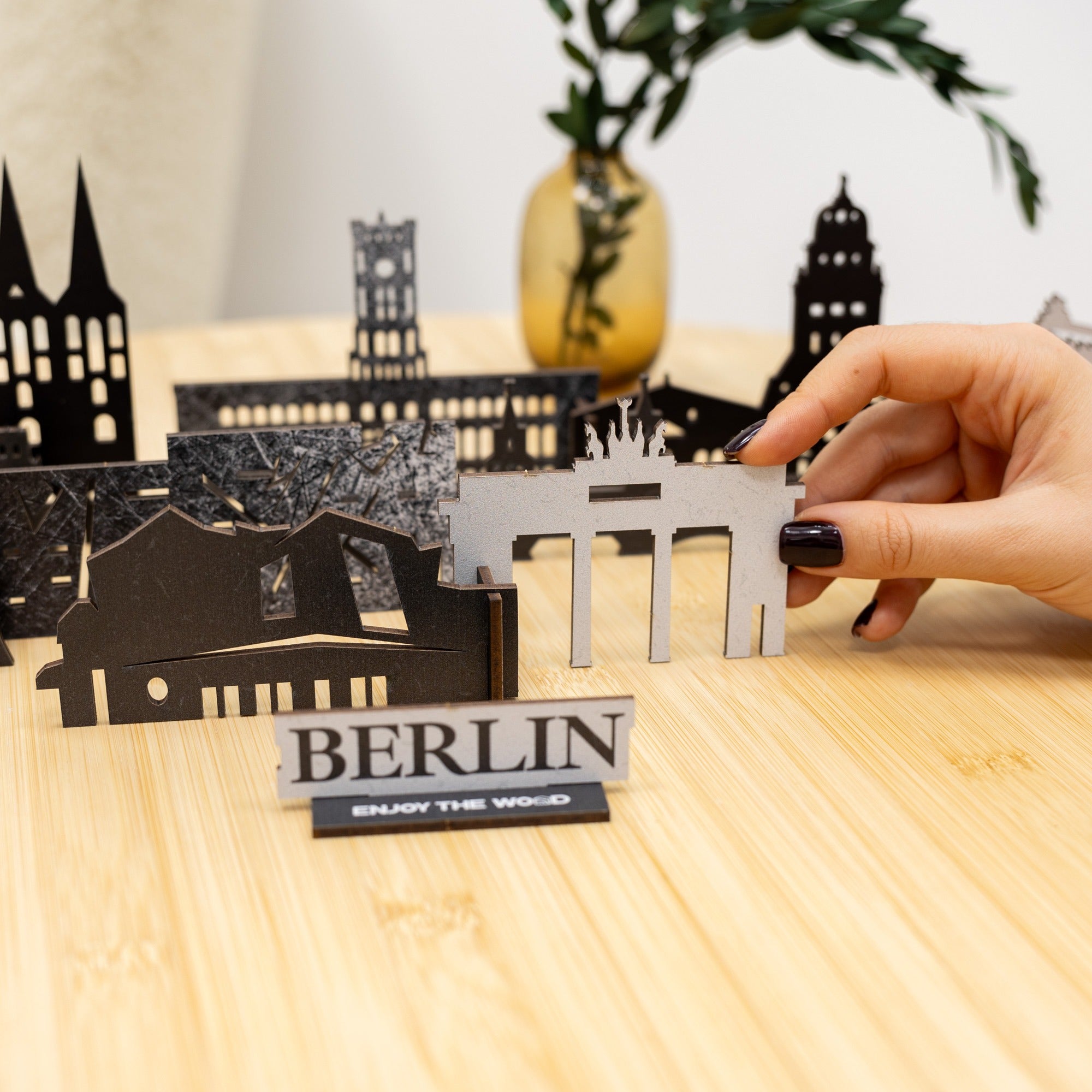 Hand holding a metal model of a building with 'BERLIN' sign on a wooden surface
