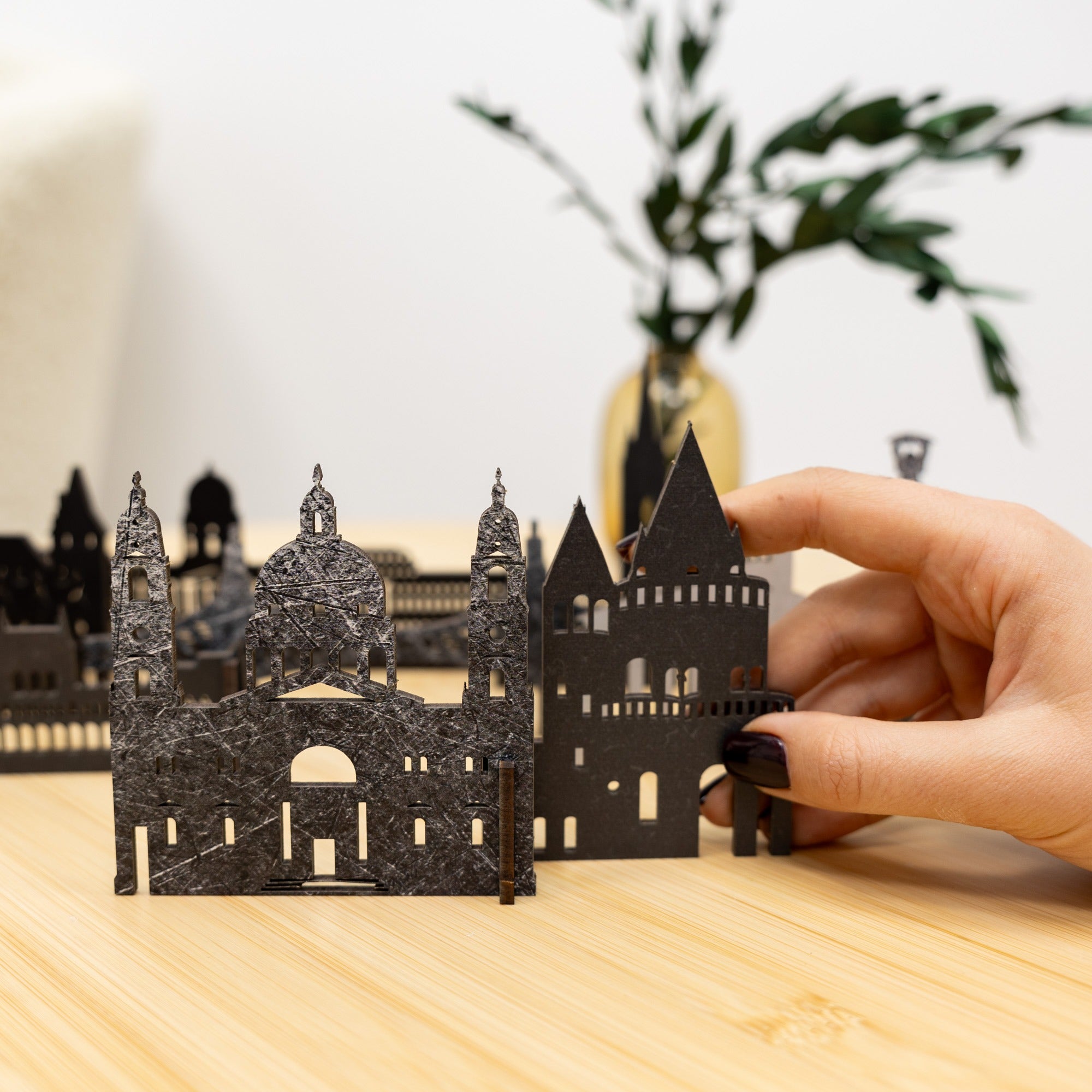 Hand holding a miniature black architectural model on a wooden surface with blurred background