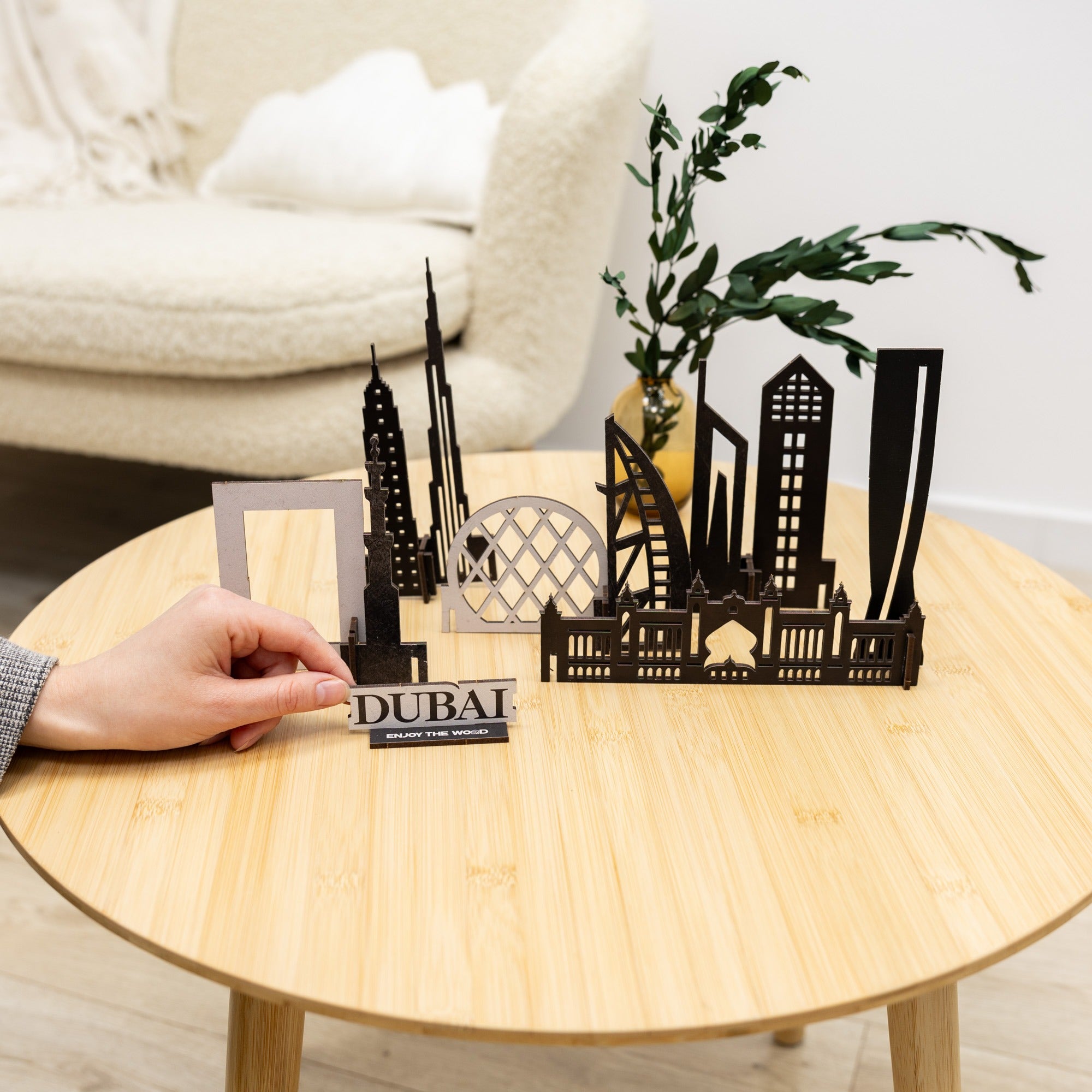 Black cut-out cityscape model of Dubai on a wooden table with a hand holding a sign that reads 'Dubai'.