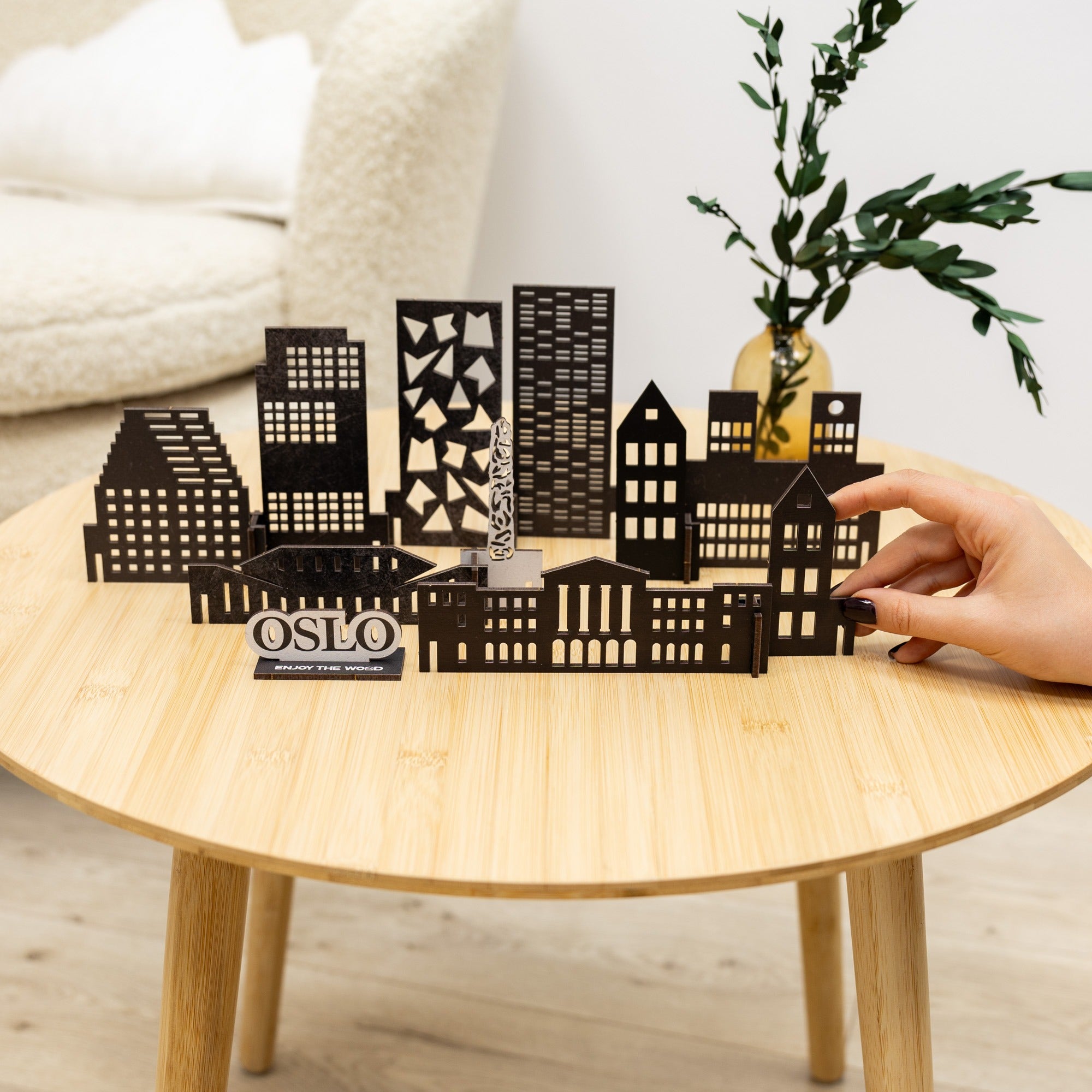 Black metal cityscape model on a wooden table with a hand interacting with it