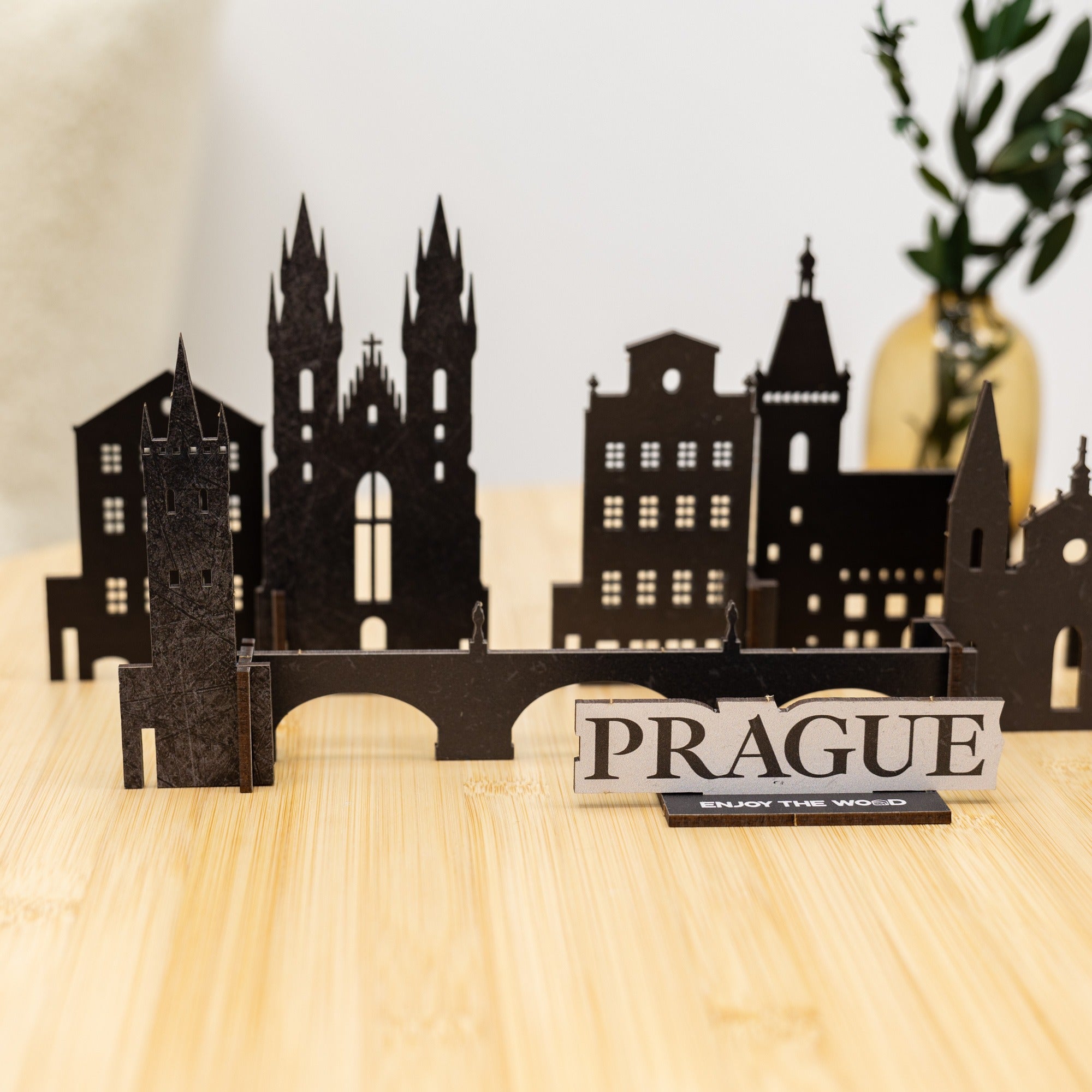 Black cutout cityscape of Prague on a wooden surface with 'PRAGUE' sign.