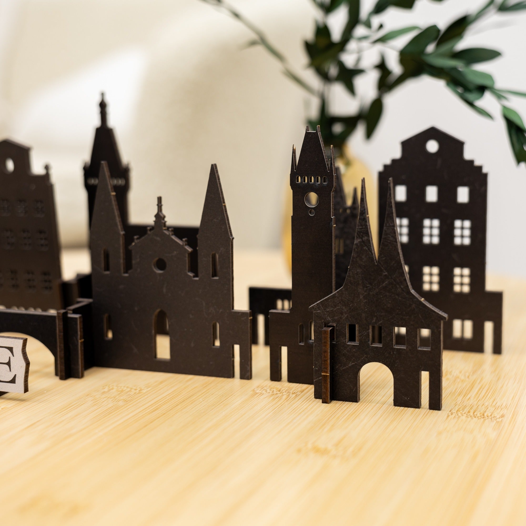 Black cut-out cityscape model on a wooden surface with a plant in the background
