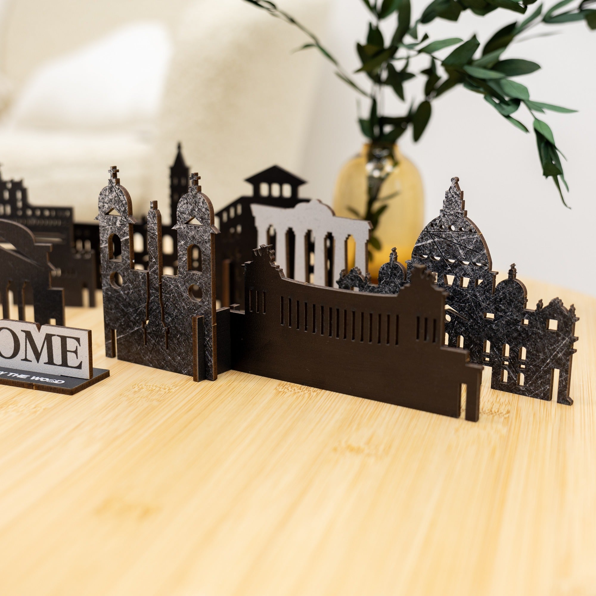 Black metal model of a cityscape on a wooden surface with a plant in the background