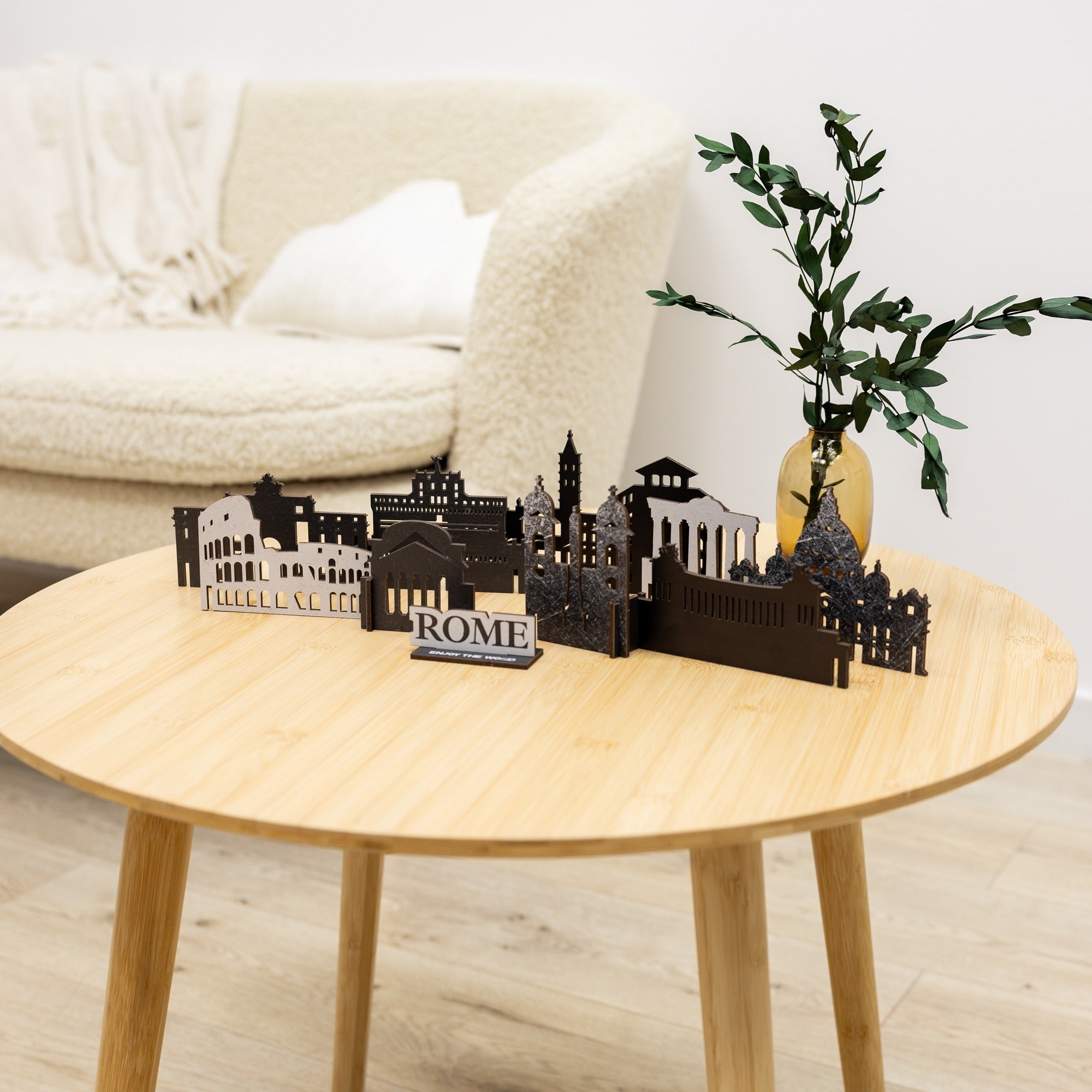 Decorative model of Roman architecture on a wooden table with a plant and white sofa in the background.