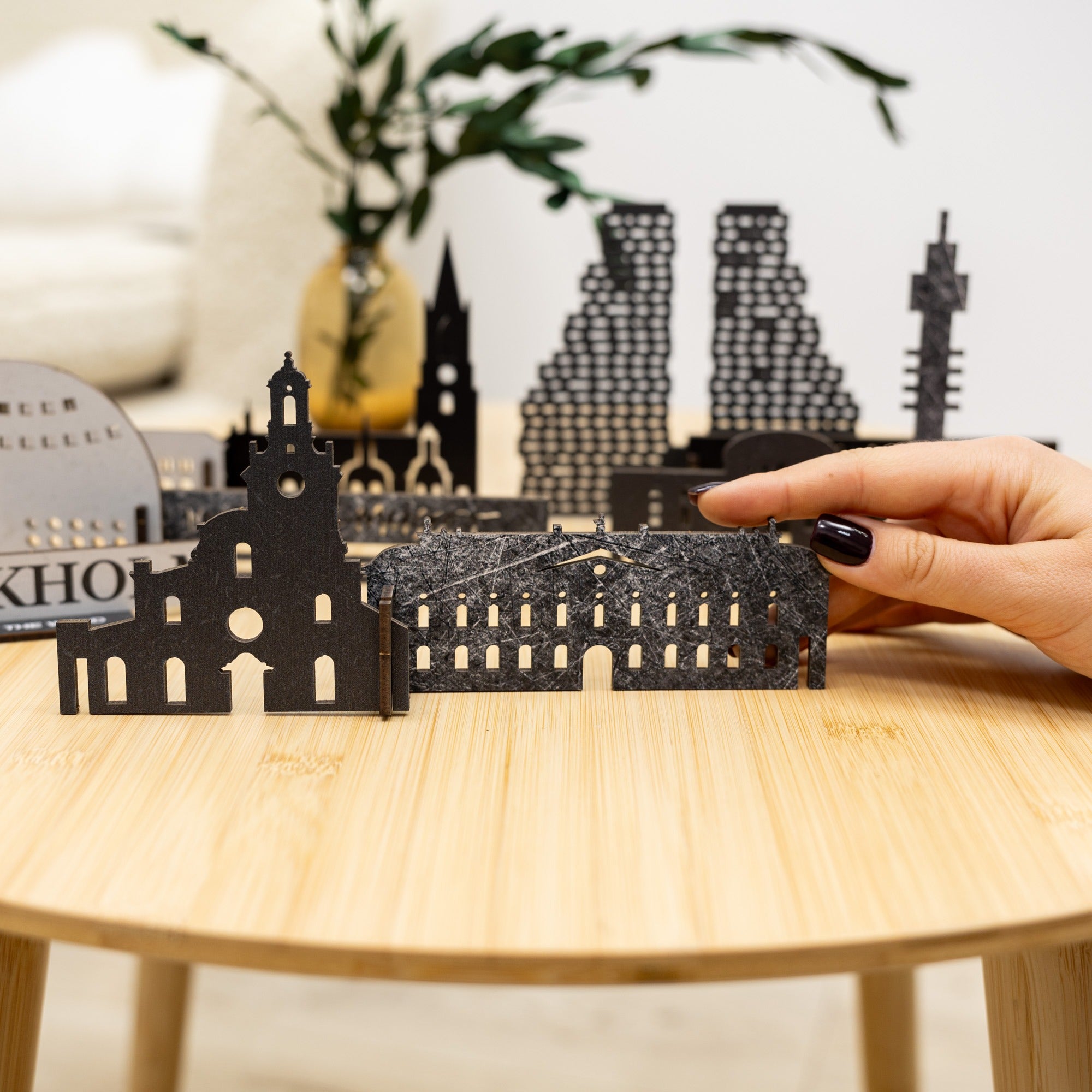 Hand holding a black metal model of a building on a wooden table with more models in the background.