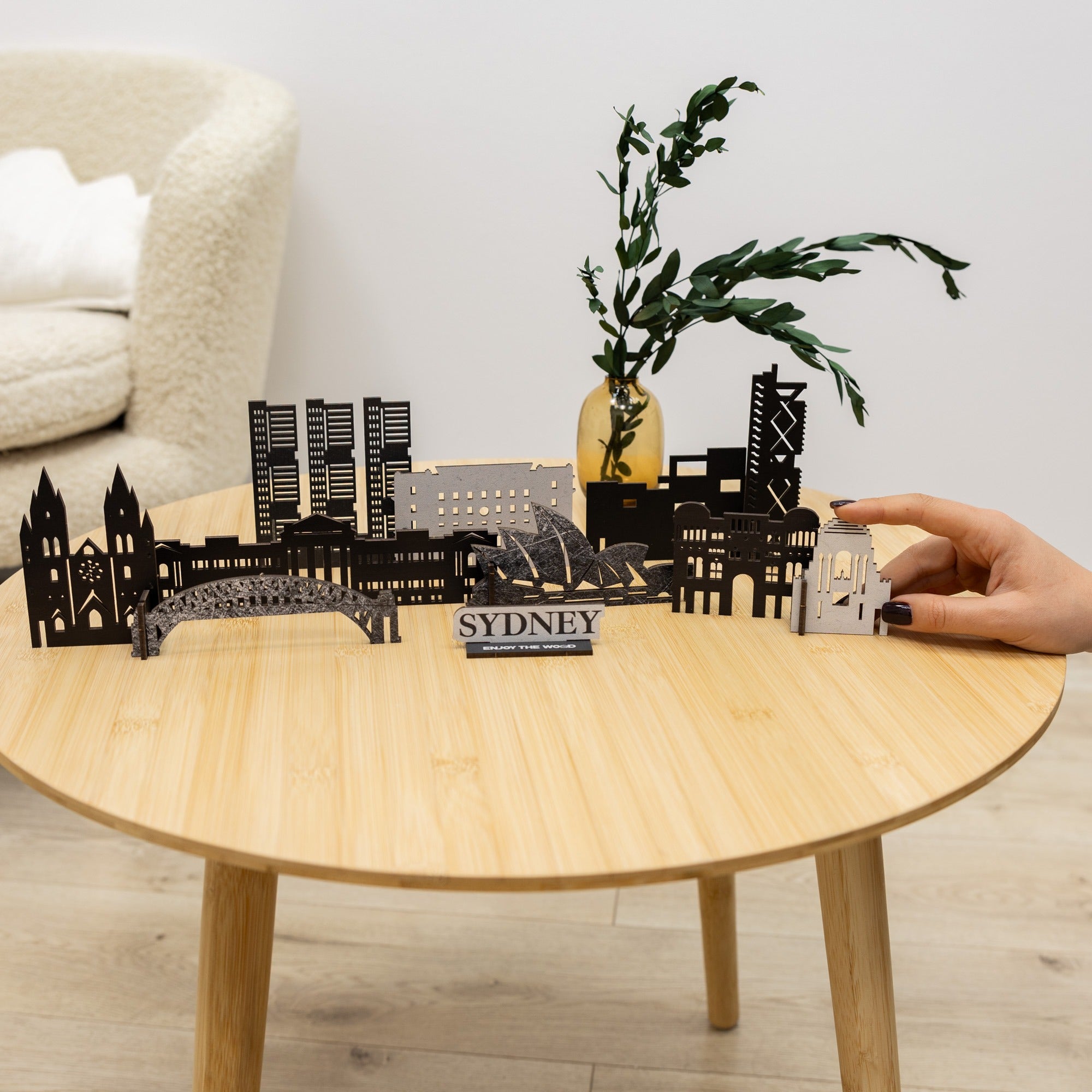 Model of a city skyline on a wooden table with a hand holding a smaller model.