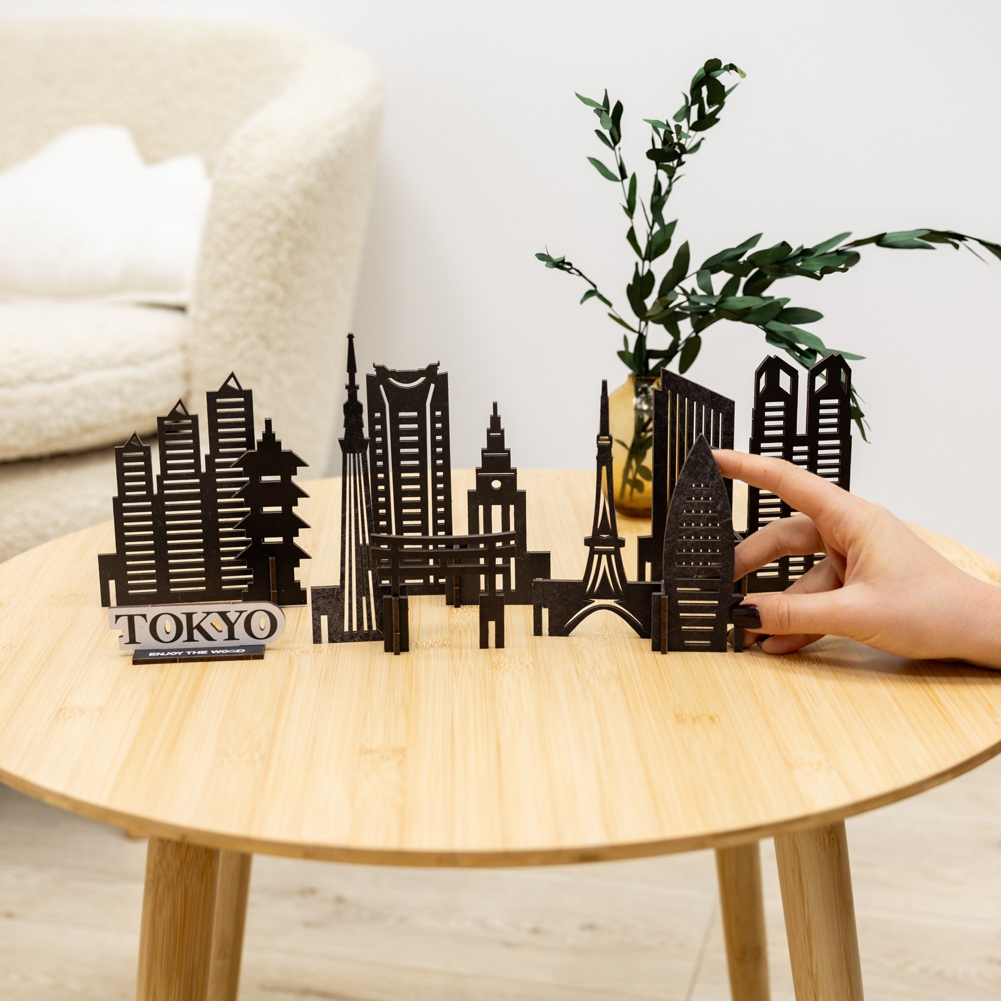 Black metal cityscape model on a wooden table with a hand reaching out