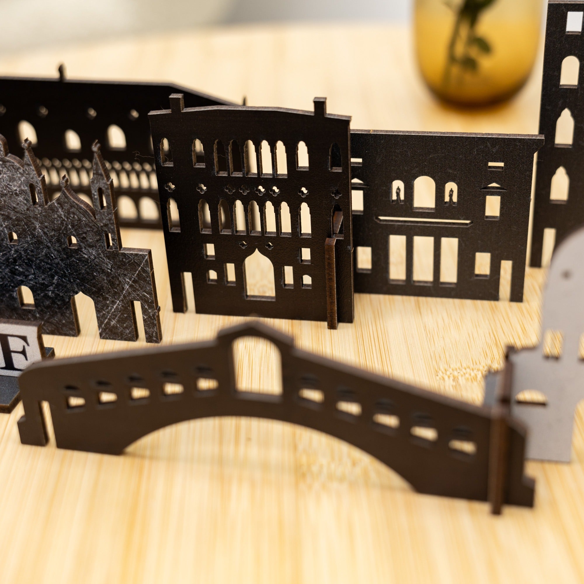 Black architectural models of buildings and a bridge on a wooden surface