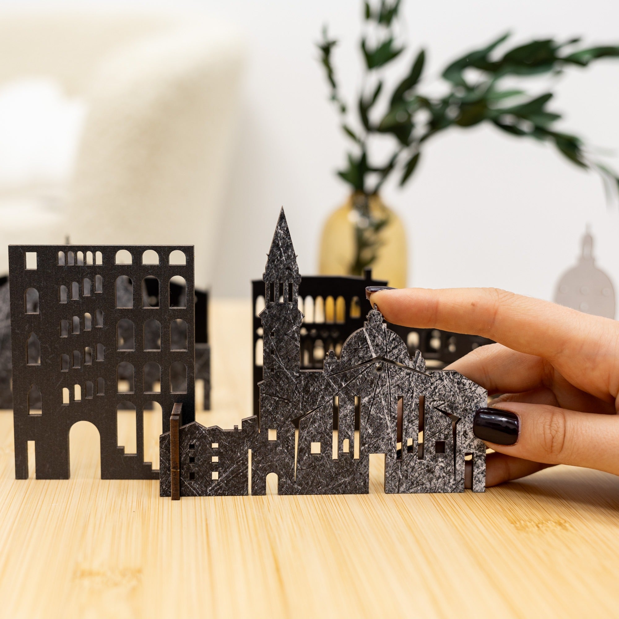 Hand holding a metallic cityscape model on a wooden surface with a blurred background