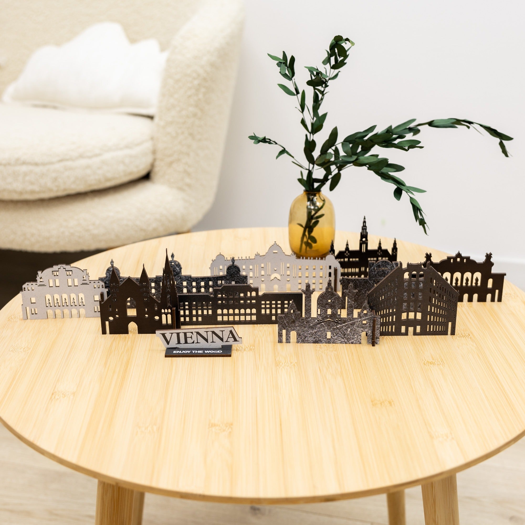 Decorative cityscape model of Vienna on a wooden table with a vase and branches.