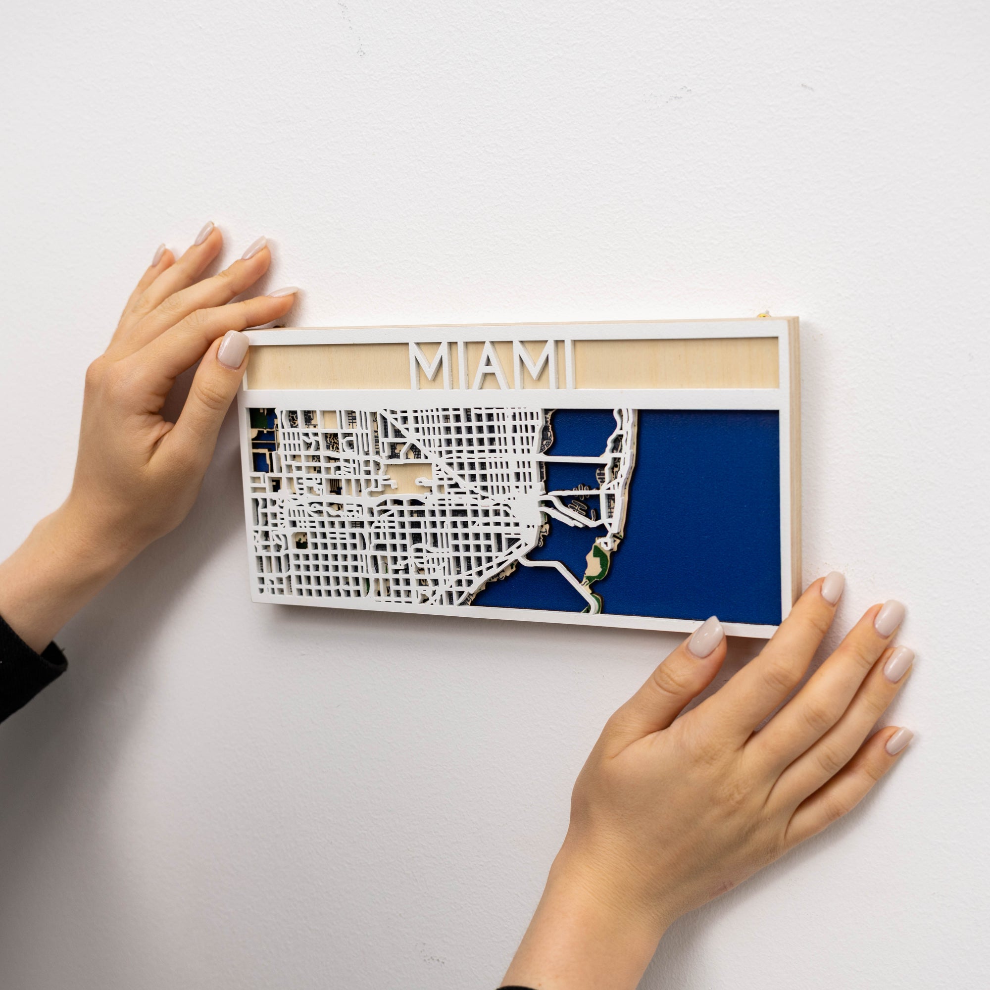 Hands holding a framed map of Miami on a white background