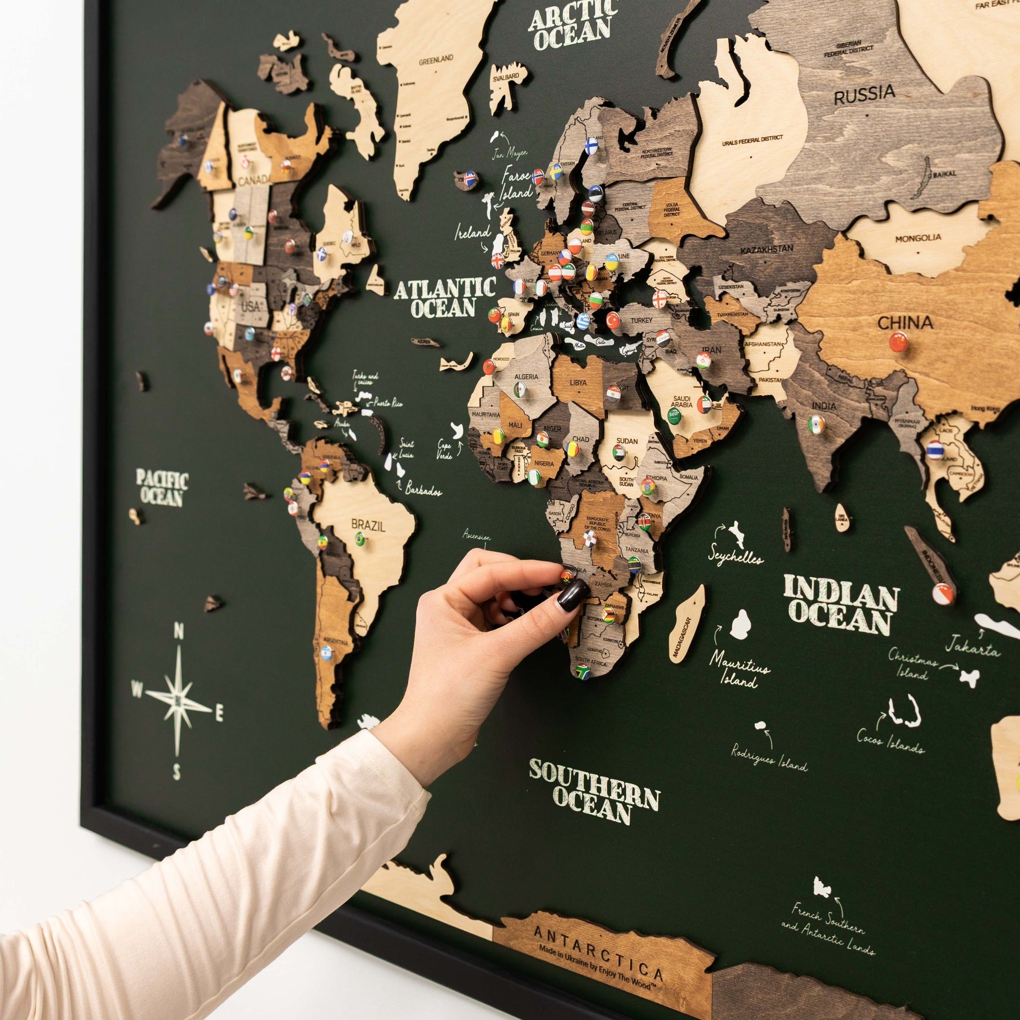 Wooden world map with a hand placing a piece on it against a dark background