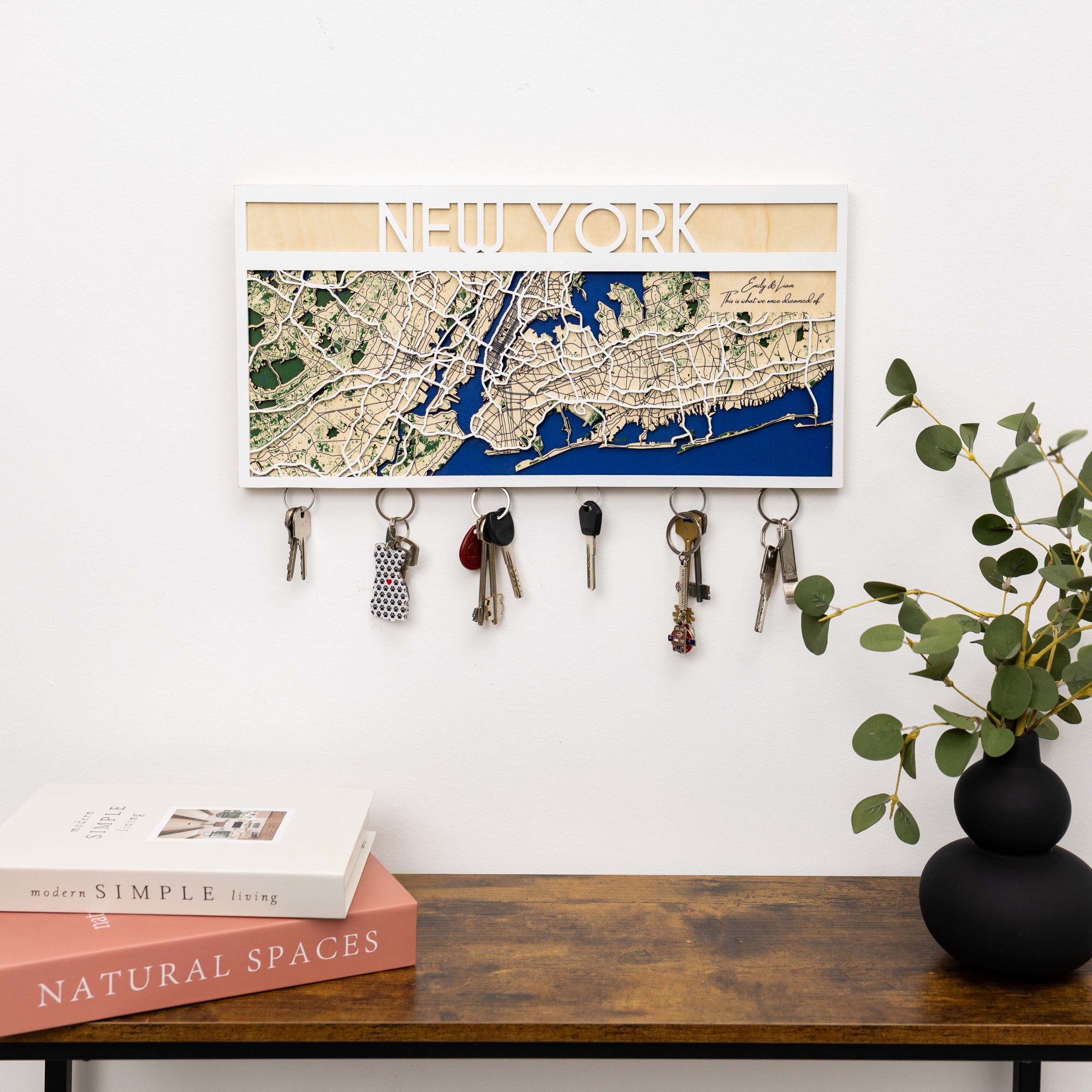Framed map of New York on a wall above a wooden surface with books and a plant.