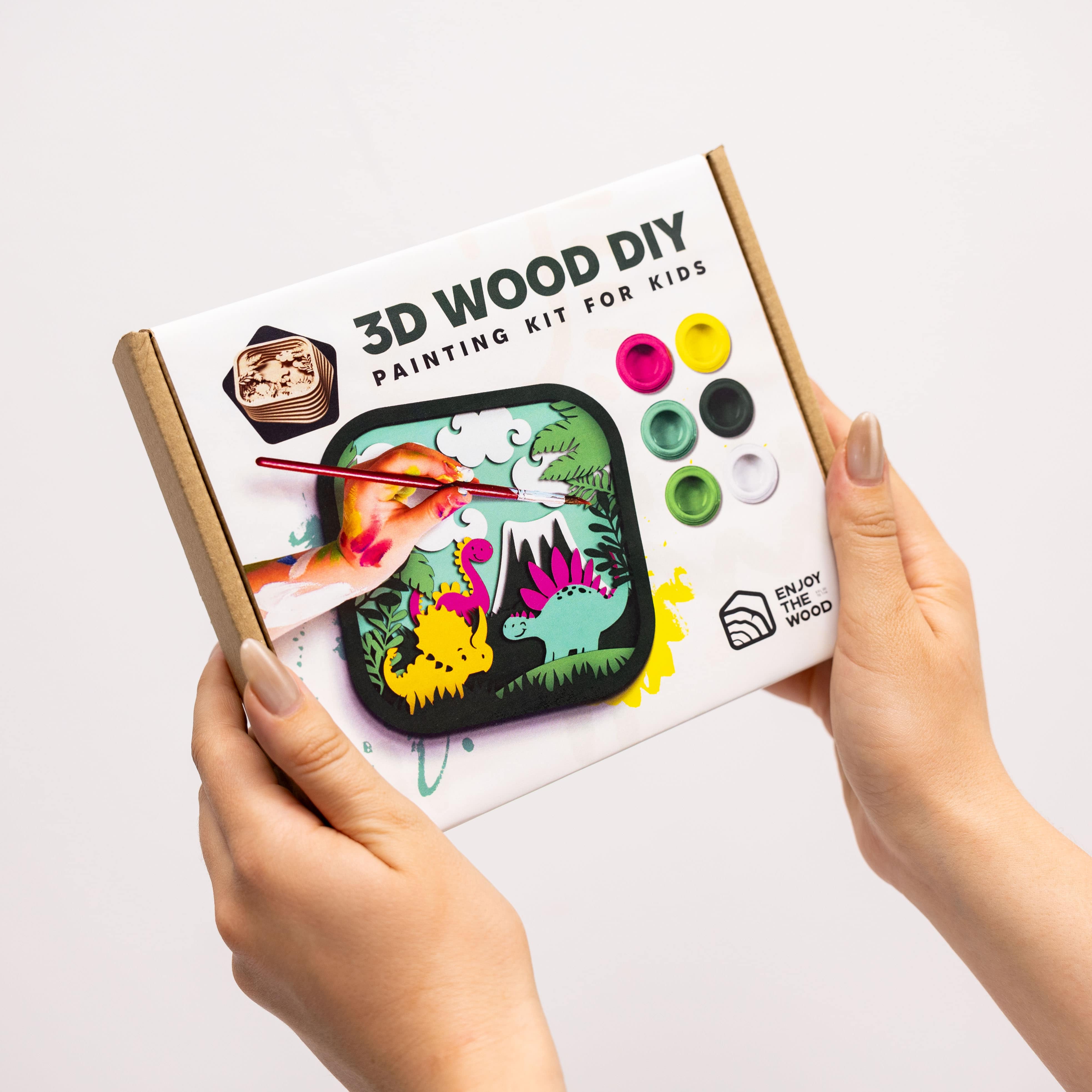 3D Wood DIY painting kit for kids held by hands on a light gray background