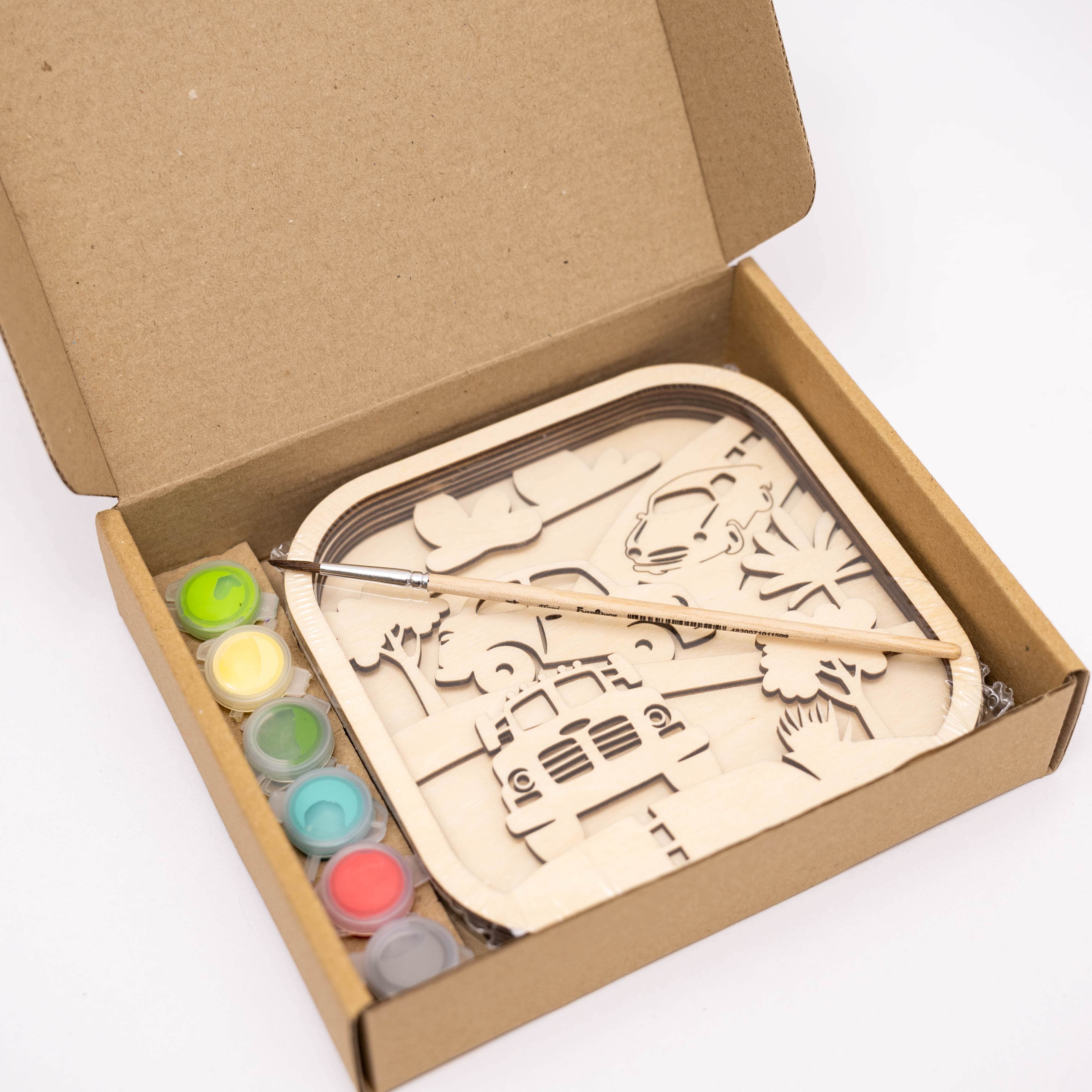 Wooden puzzle with paint and brush in a cardboard box on a white background