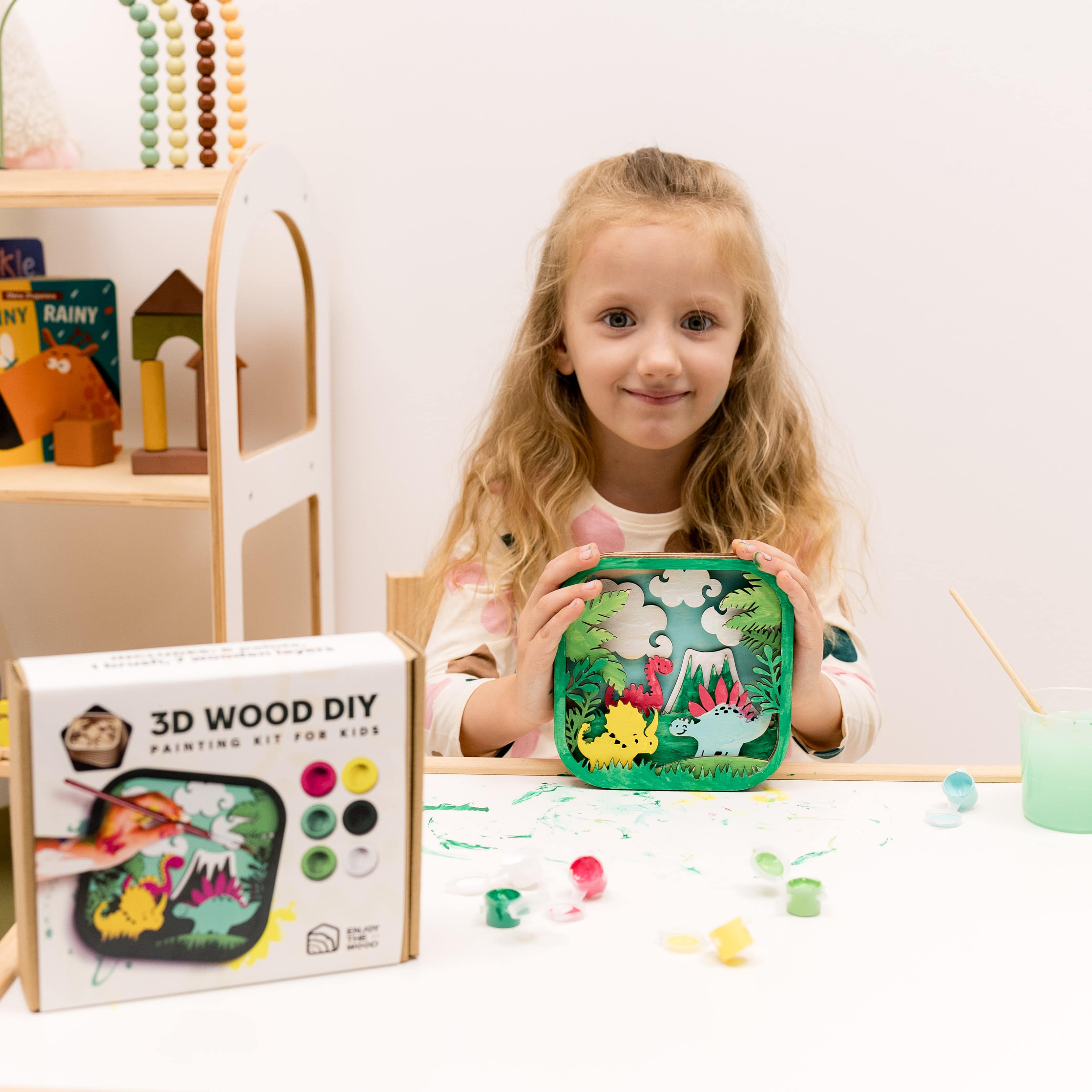Child holding a 3D wood DIY painting kit with a colorful wooden shelf in the background