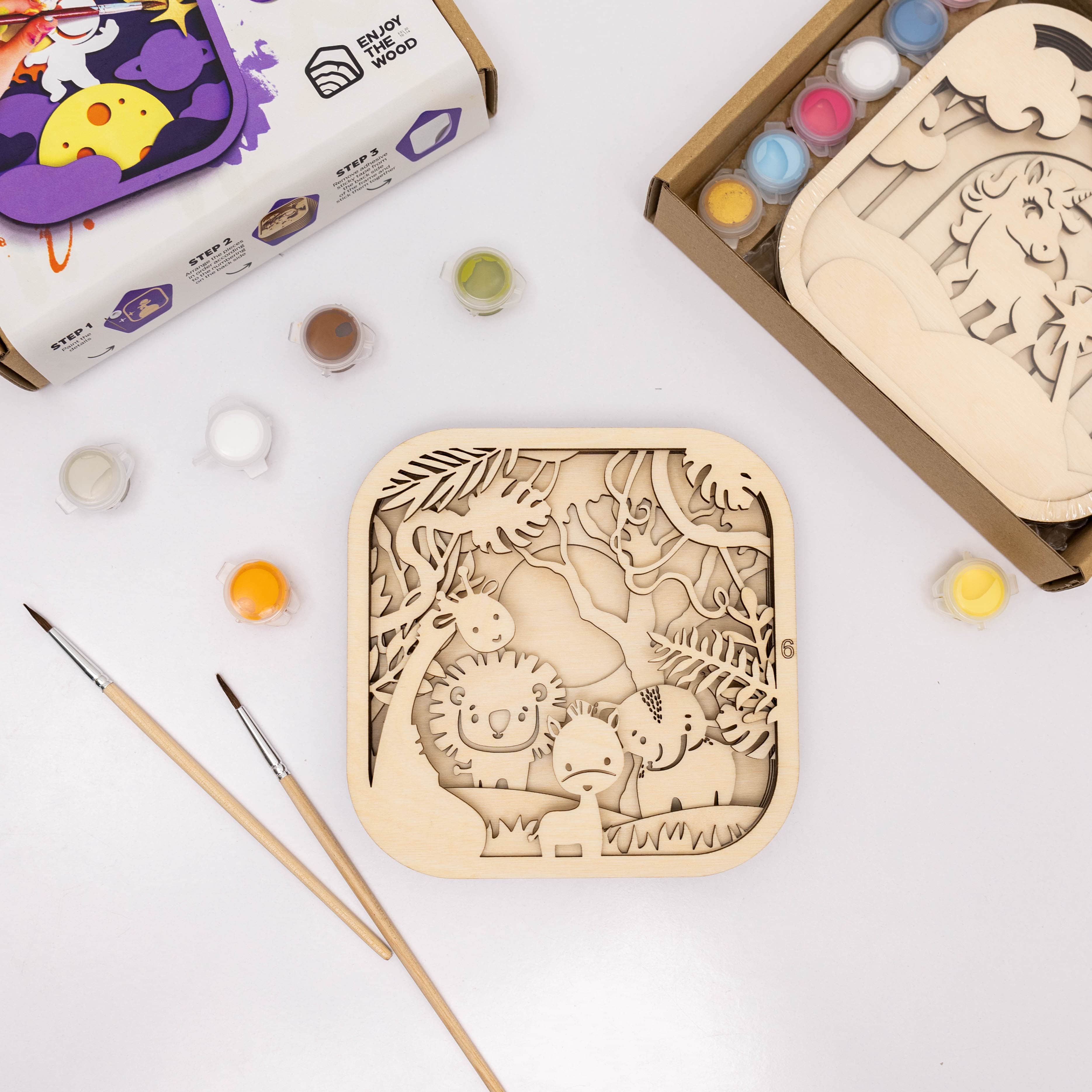 Wooden puzzle with animal designs on a white surface with paint bottles and brushes.