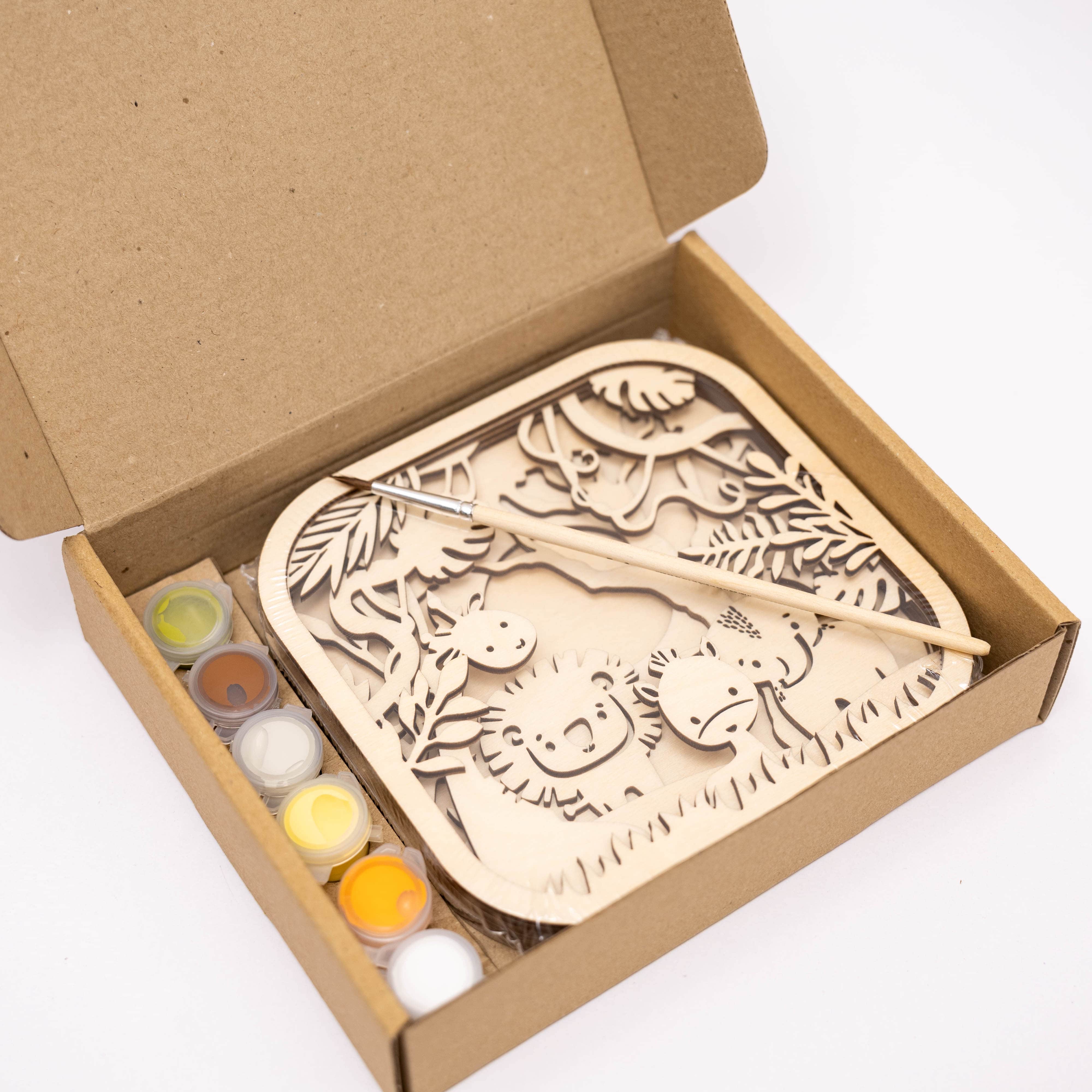 Wooden craft kit with laser-cut design and paint bottles in a cardboard box on a white background