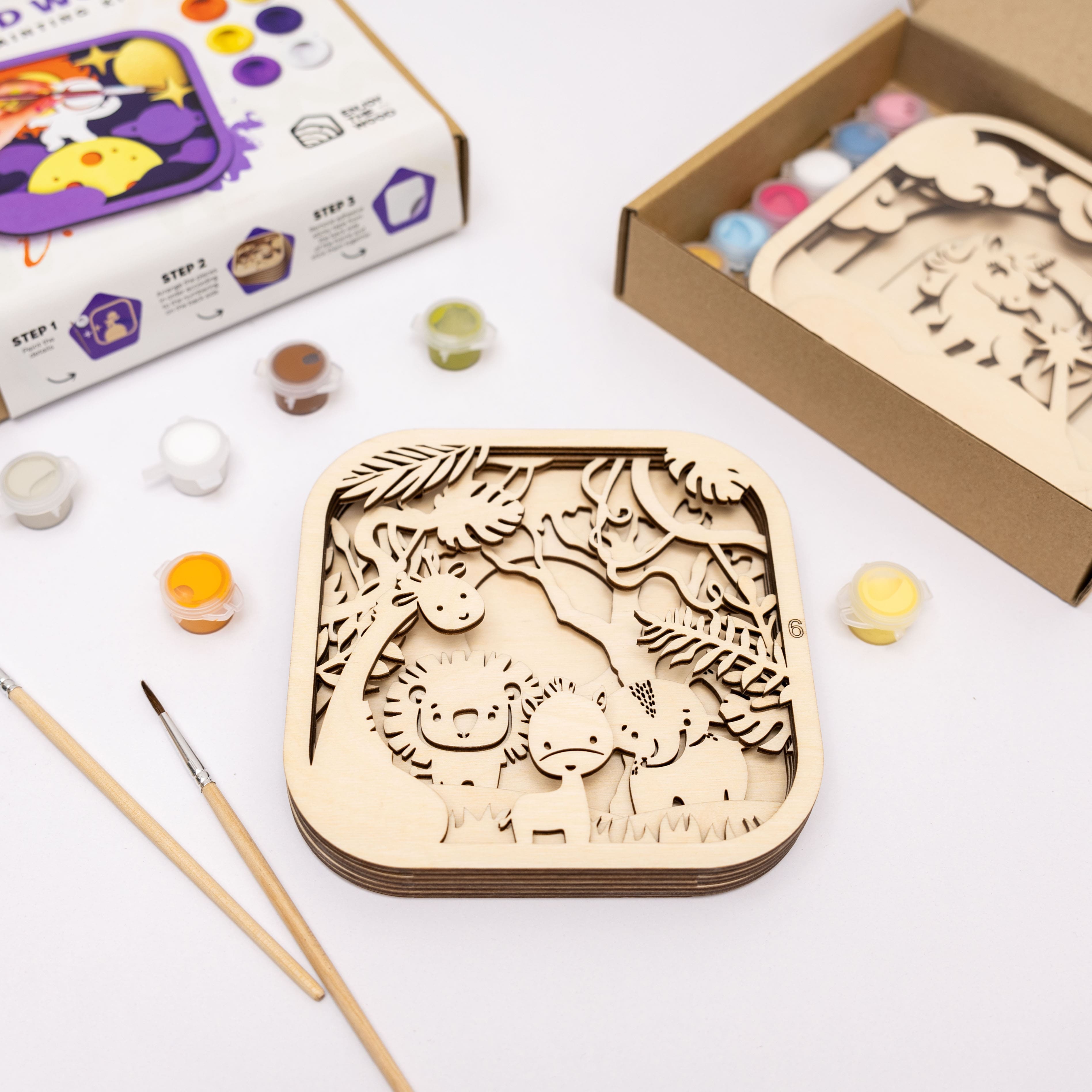 Wooden art project with paint supplies and packaging on a white surface