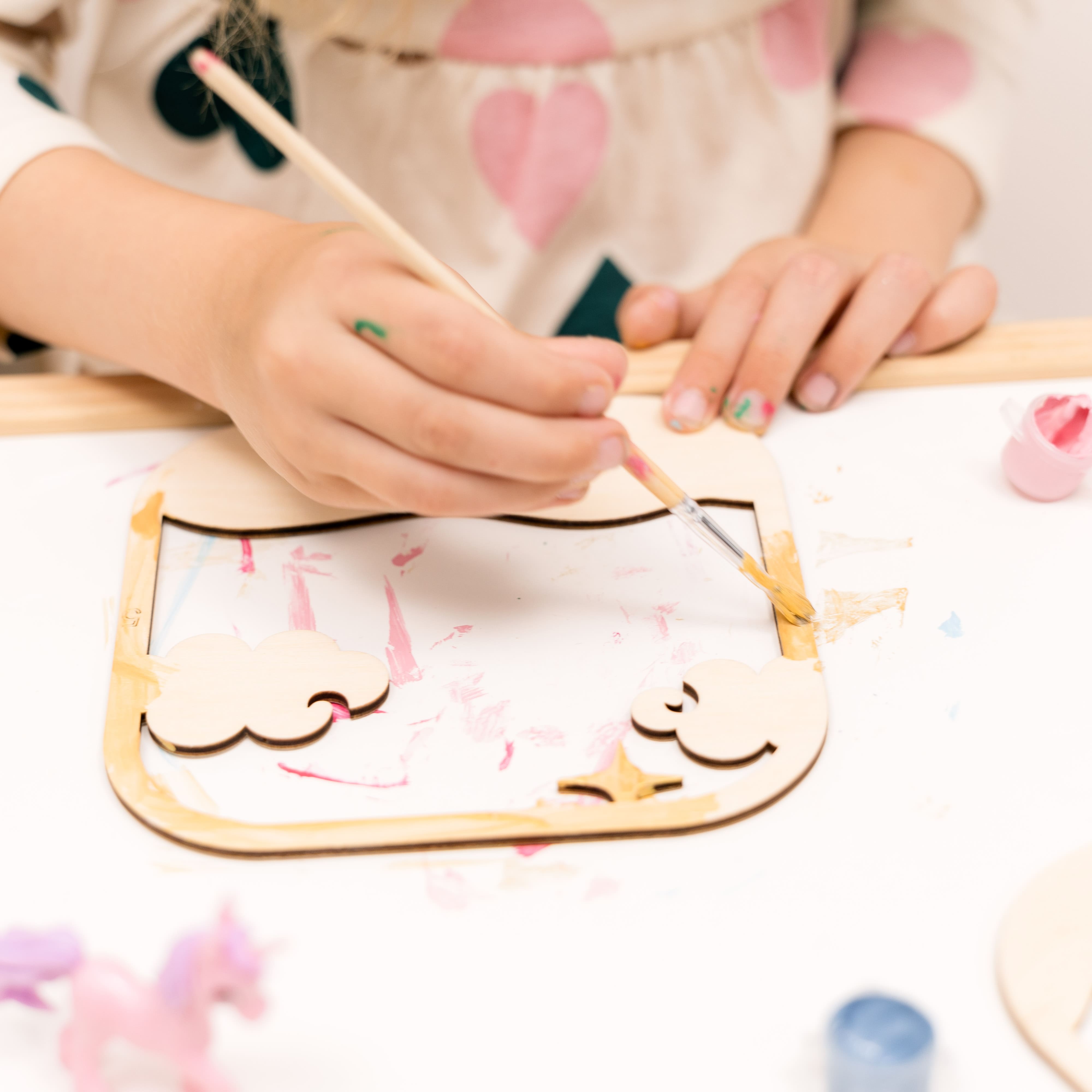 Child painting a wooden craft with paintbrushes