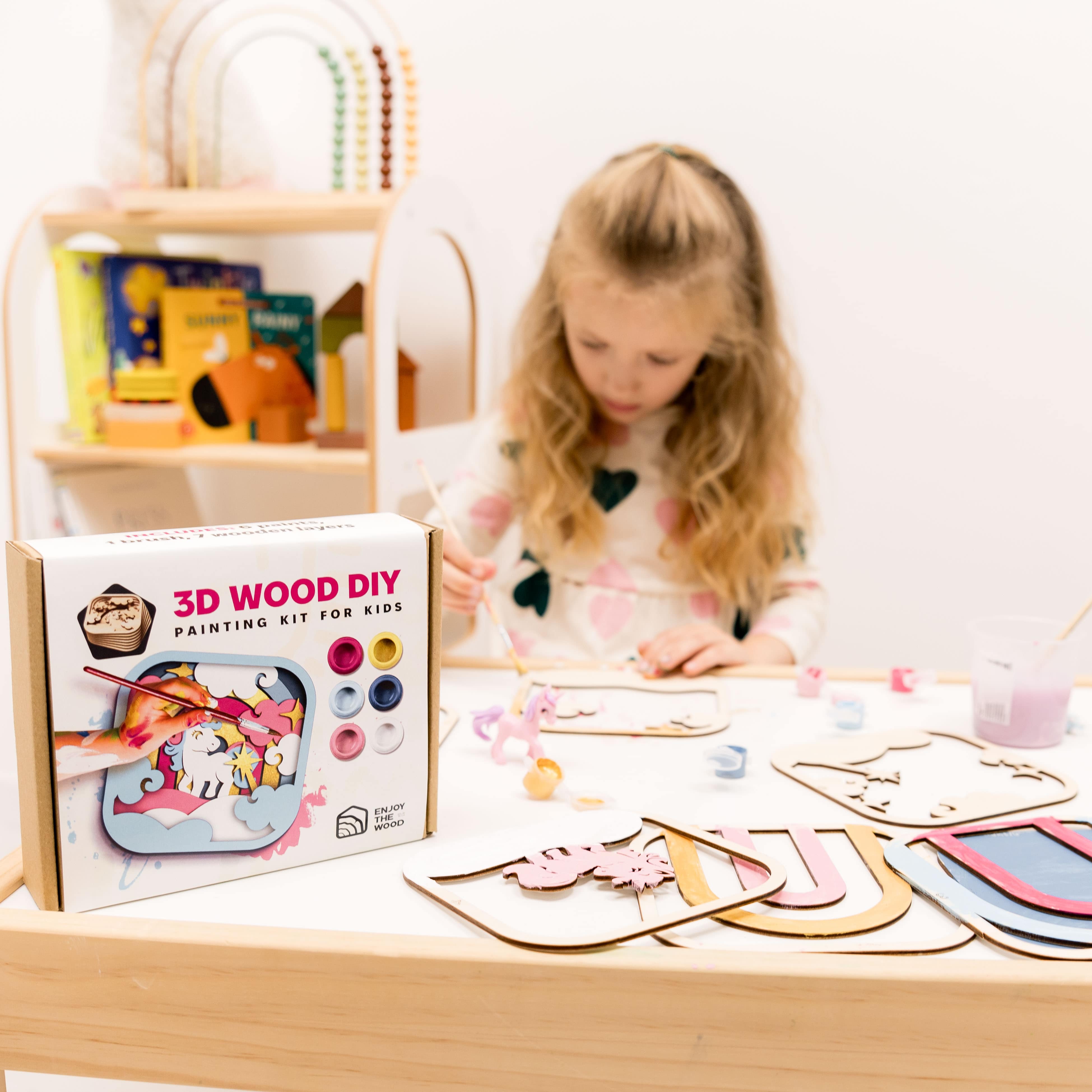 Child engaged in a 3D wood DIY painting kit for kids on a table with a box in front.