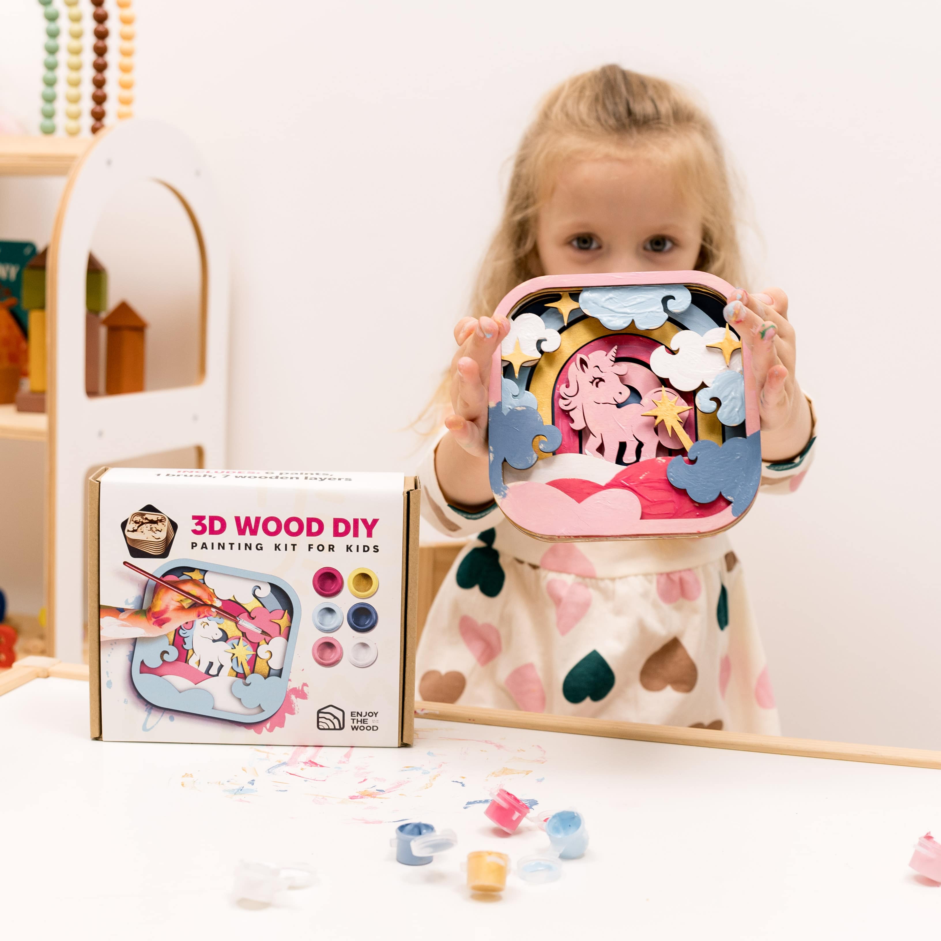 Child holding a 3D wood DIY painting kit with colorful pieces and packaging.