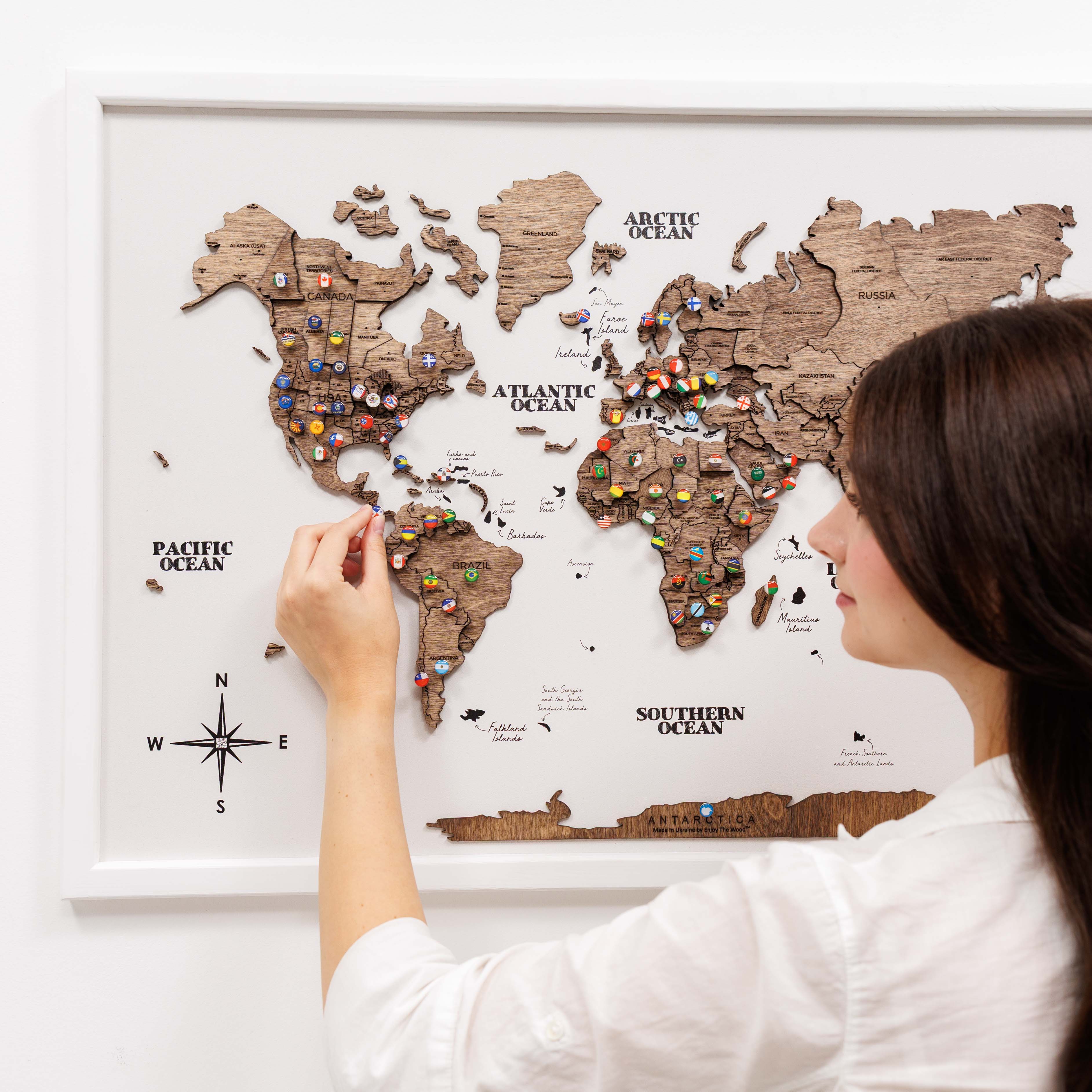 Woman interacting with a wooden world map on a white wall