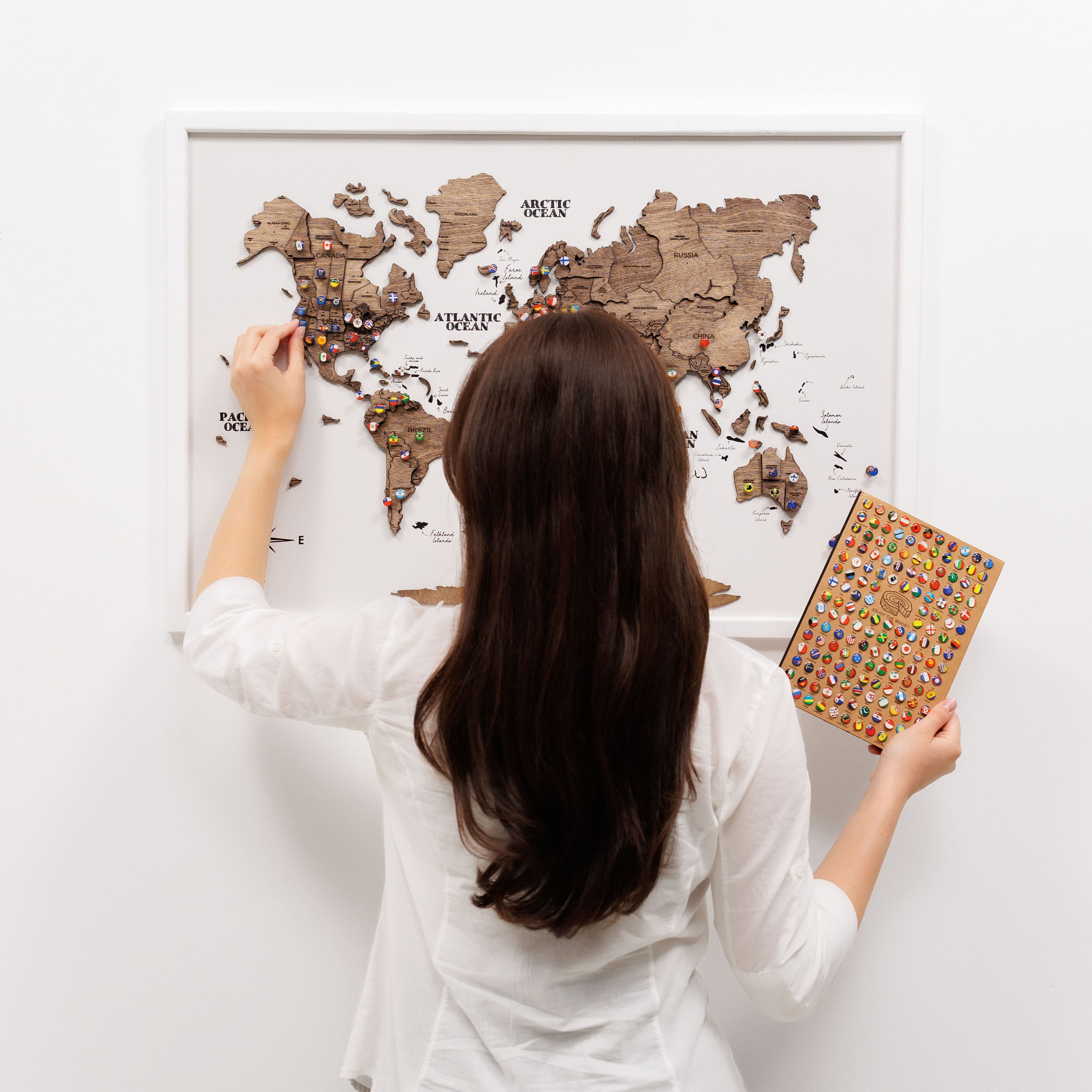 Woman assembling a wooden world map puzzle on a white wall.
