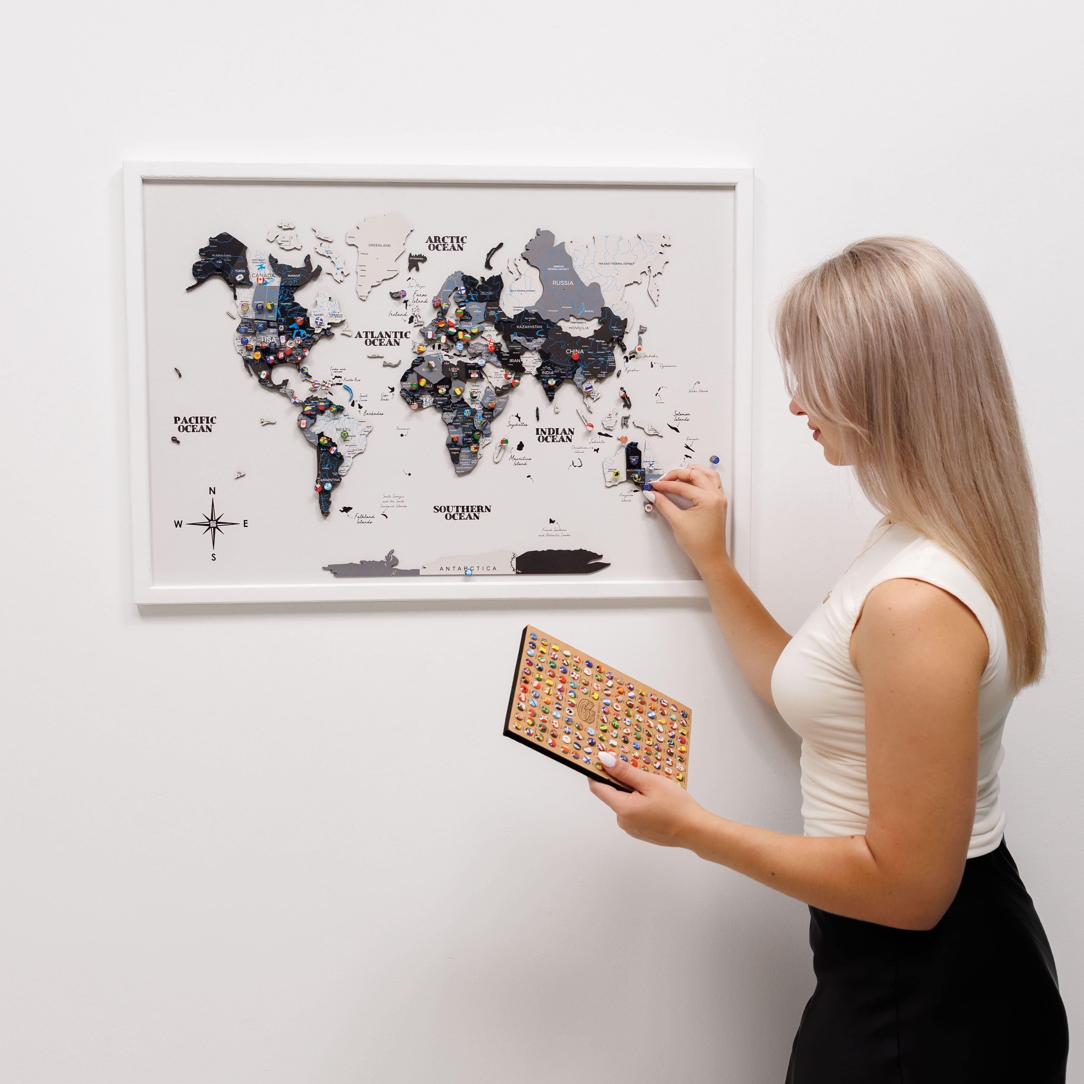 Woman holding a framed world map puzzle against a white wall