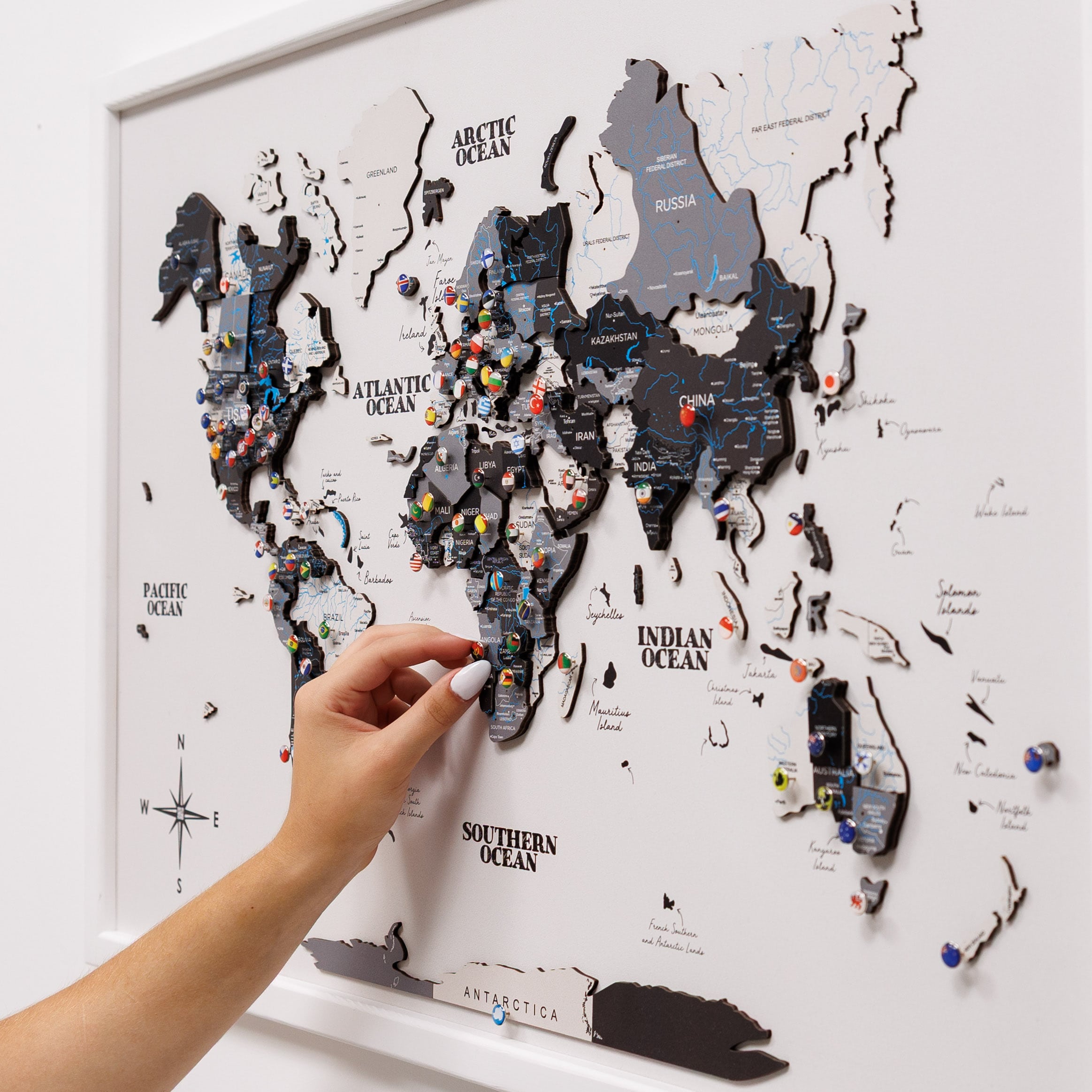 World map with pins on a white wall, hand placing a pin.