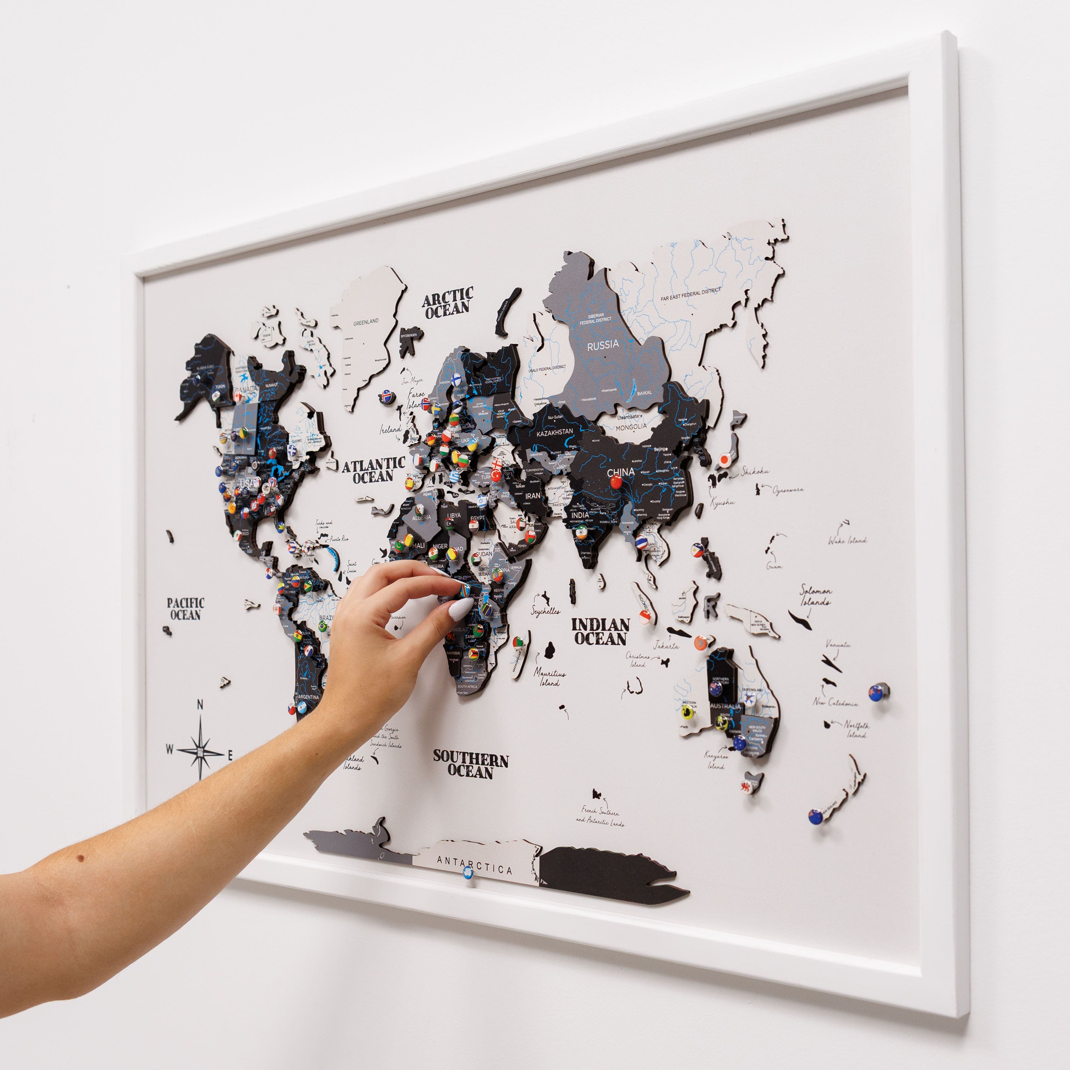 World map with pins on a white wall, hand reaching to add a pin.