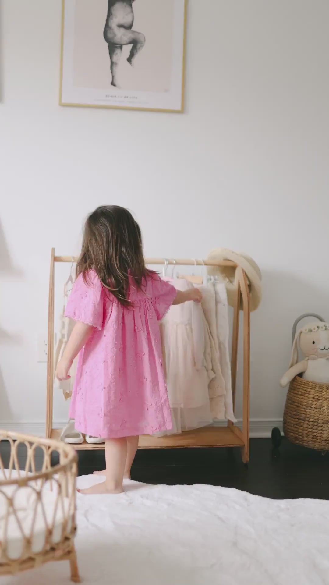 Little girl in pink dress choosing clothes from rack