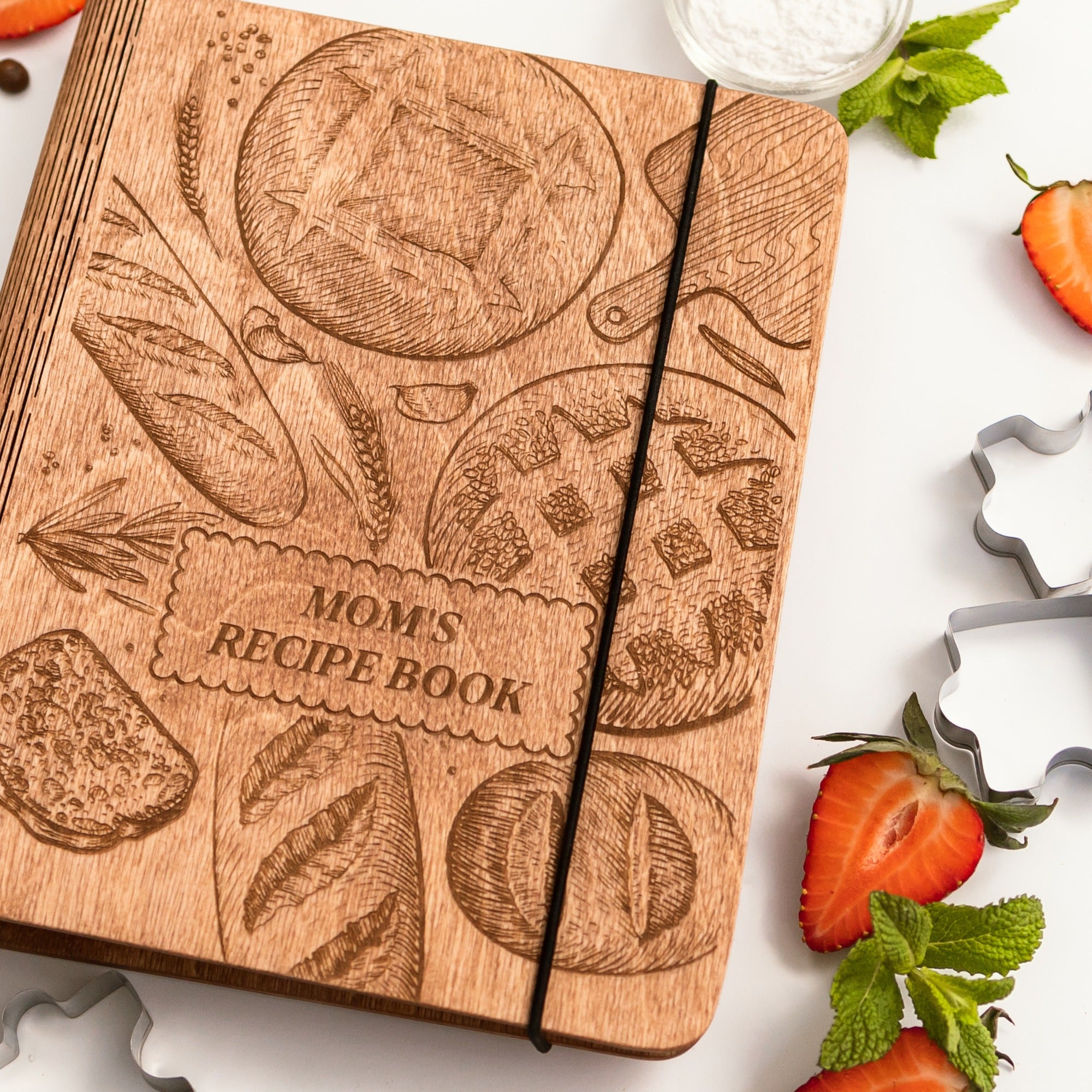 Wooden recipe book titled 'Mom's Recipe Book' with kitchen-themed designs on a white background.