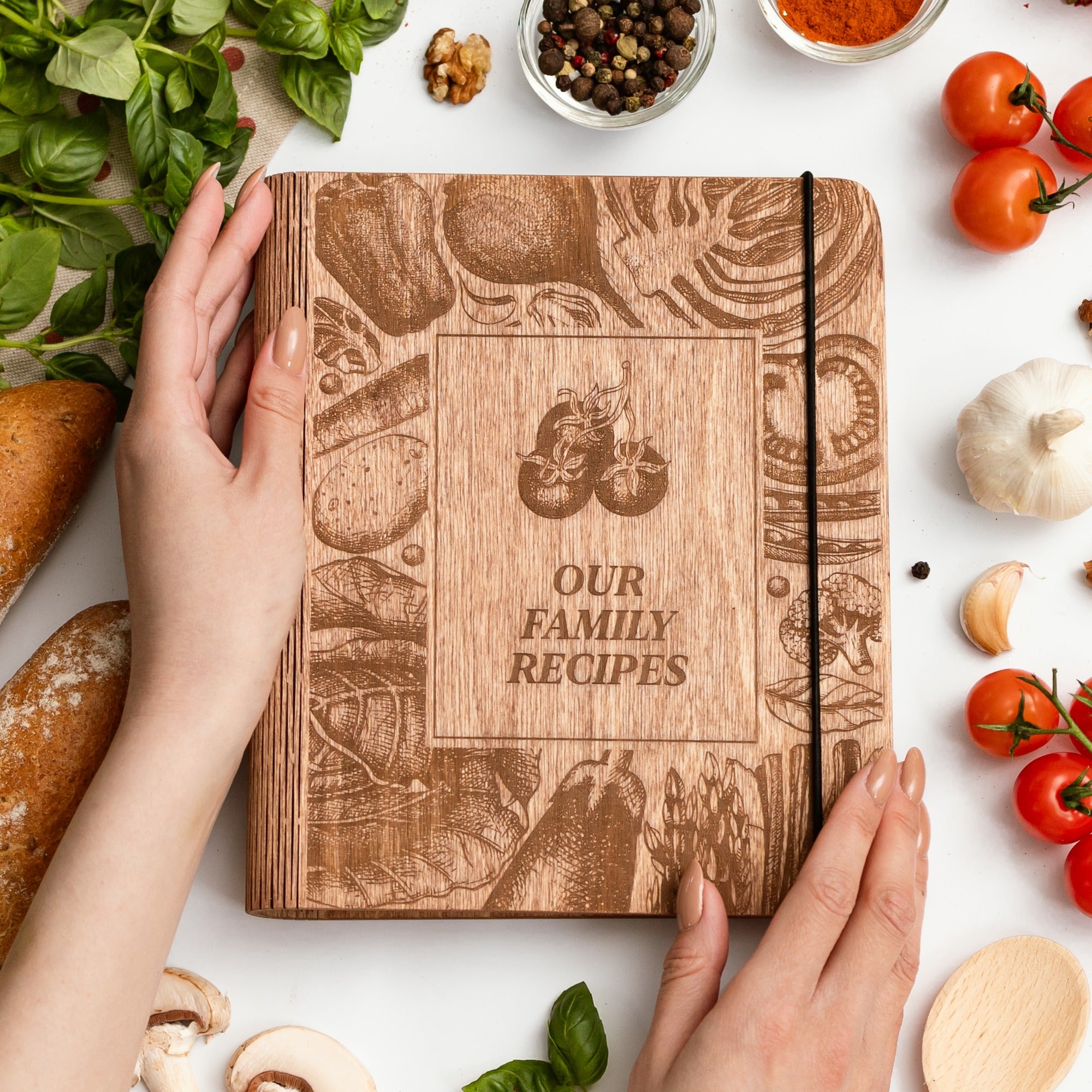 Wooden recipe book titled 'Our Family Recipes' surrounded by kitchen items on a white surface