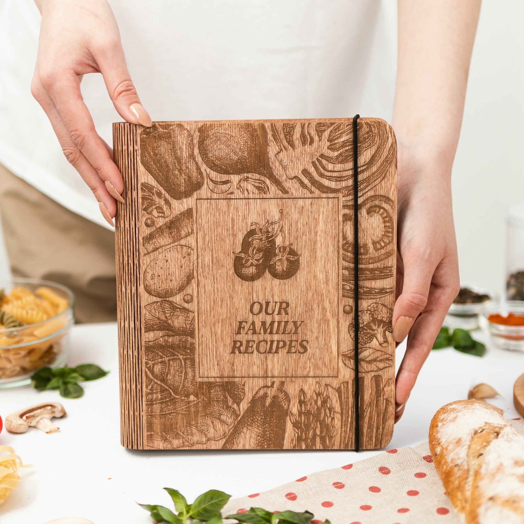 Wooden recipe book titled 'Our Family Recipes' held by a person with food items in the background.