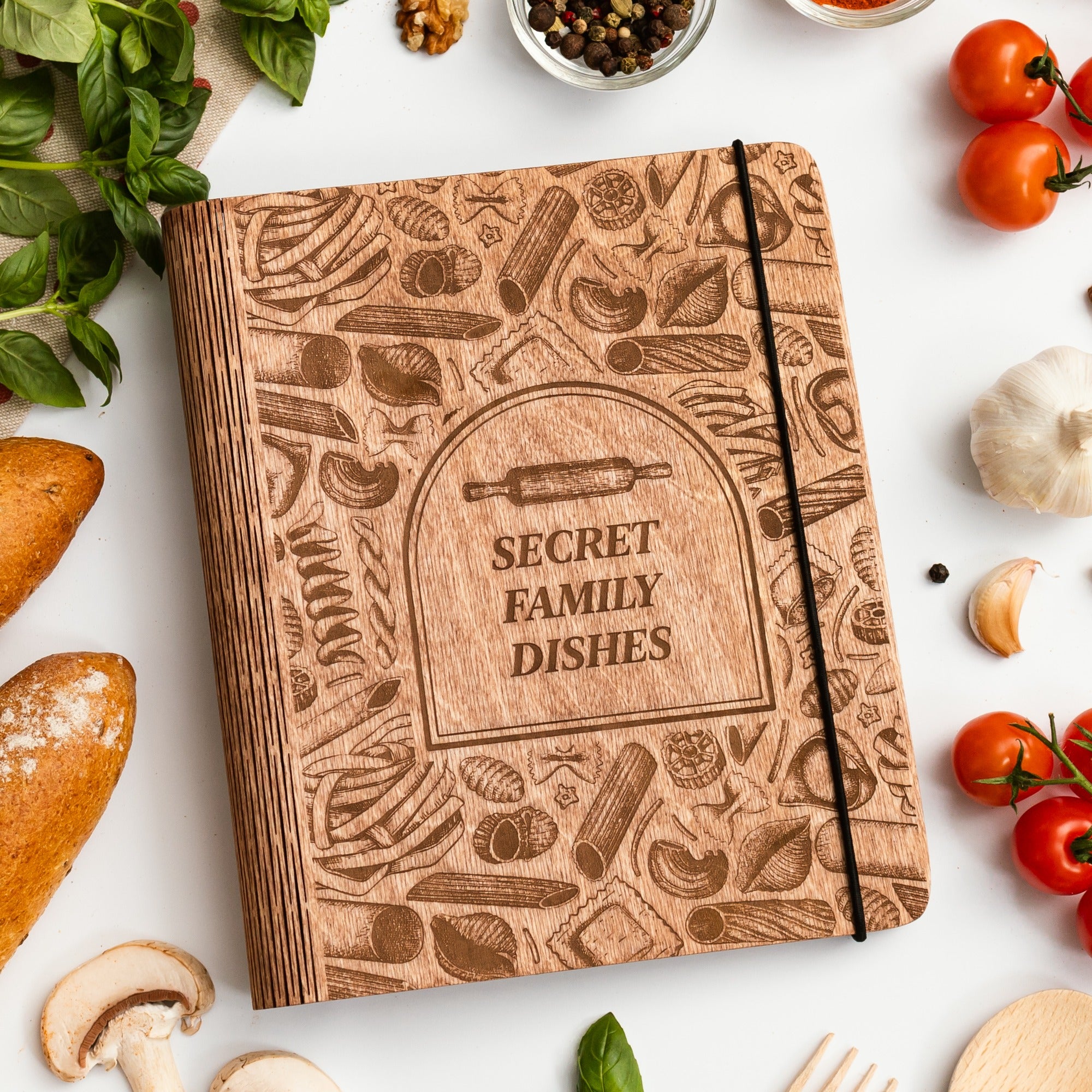 Wooden notebook titled 'Secret Family Dishes' surrounded by kitchen items on a white surface