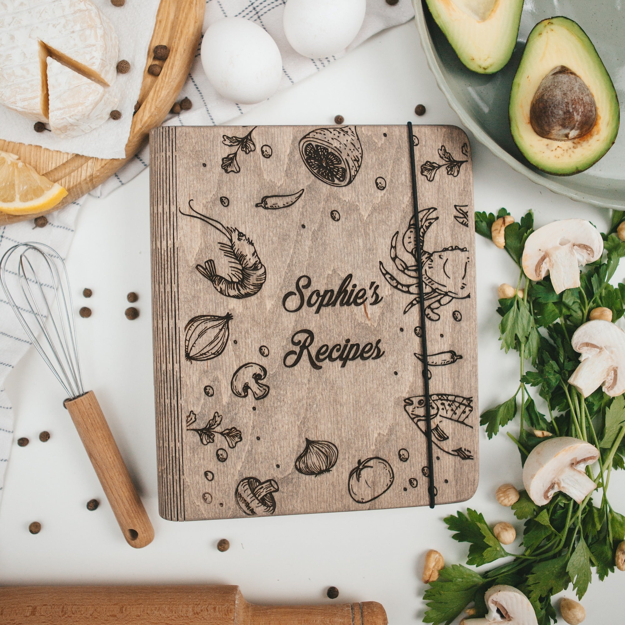 Wooden recipe book titled 'Sophie's Recipes' surrounded by kitchen items on a white surface.