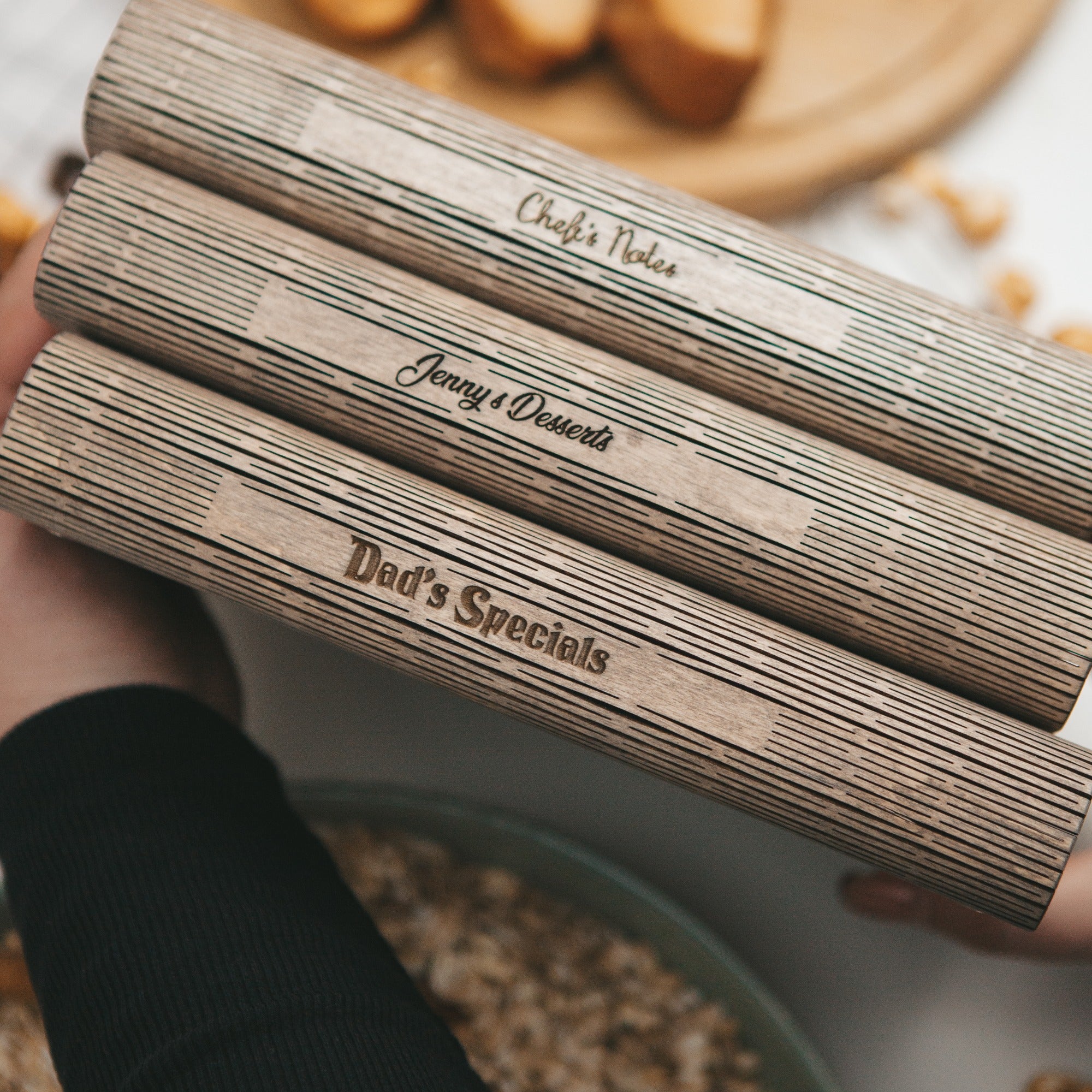 Three wooden rolling pins with engraved text held over a baking tray with ingredients.