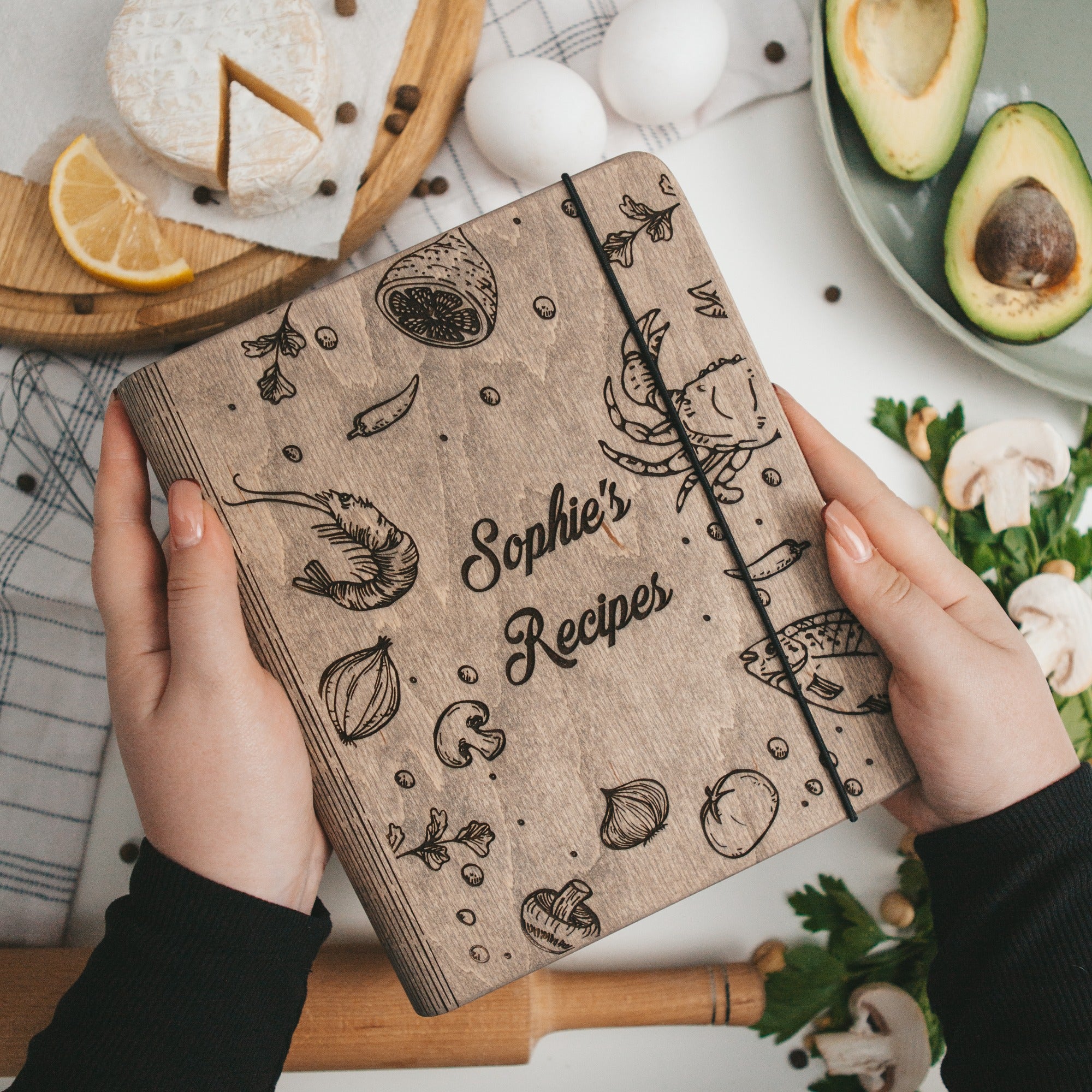 Notebook titled 'Sophie's Recipes' held by hands with kitchen items in the background