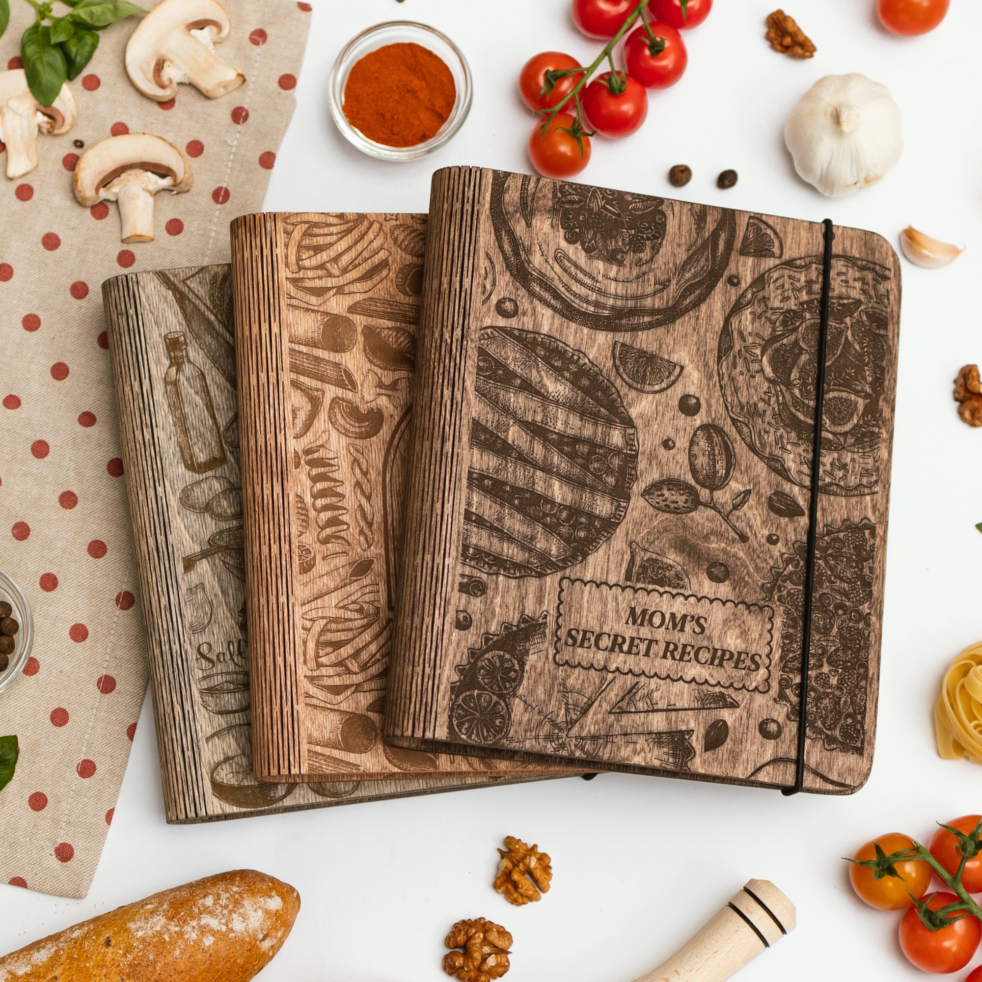 Wooden recipe books with food-themed designs on a white surface with ingredients.
